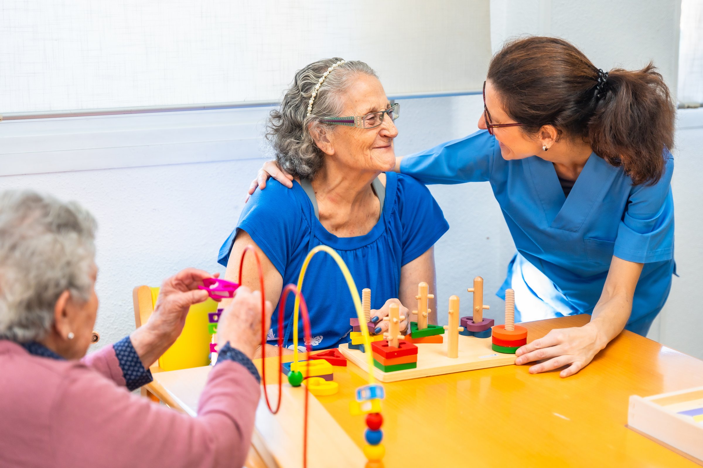 Tender caregiver assisting a senior woman while playing skill games in the nursing home