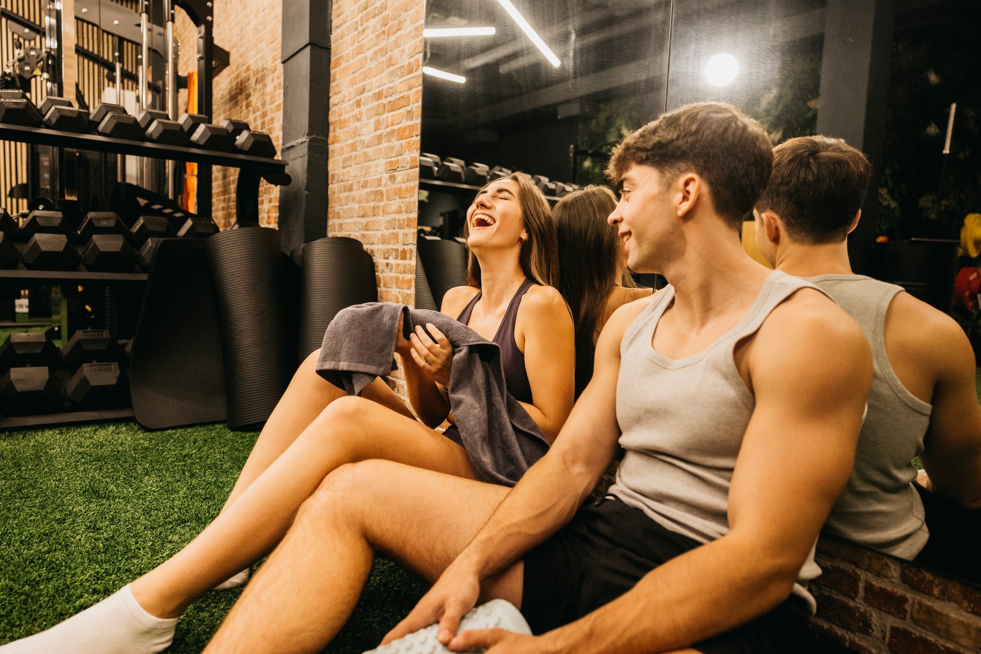 A young couple enjoys a lighthearted moment while sitting on the gym floor. They are laughing and appear relaxed after a workout session.