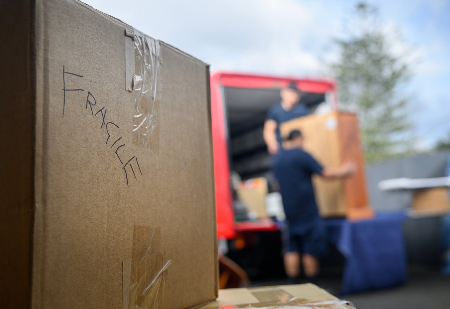 Hand-written word Fragile on the cardboard box. Unrecognizable people loading furniture to the pickup truck. Concept of home moving and delivery.