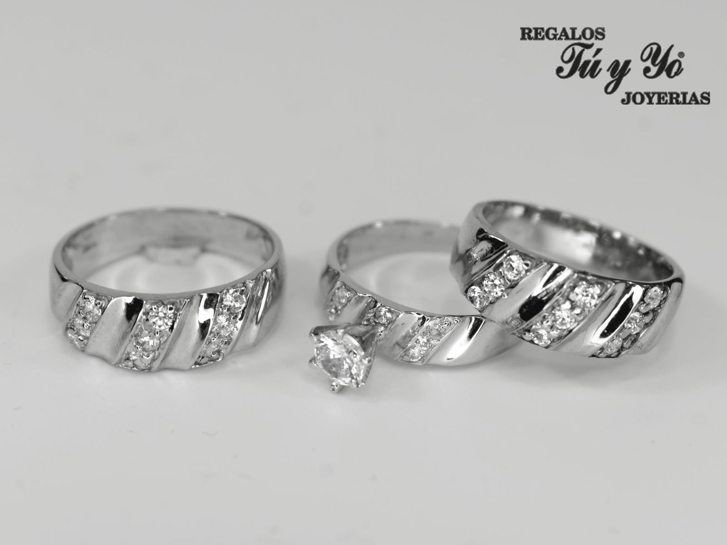 Three silver rings with diamond accents, displayed on a white surface. Branding text in Spanish is visible in the corner.