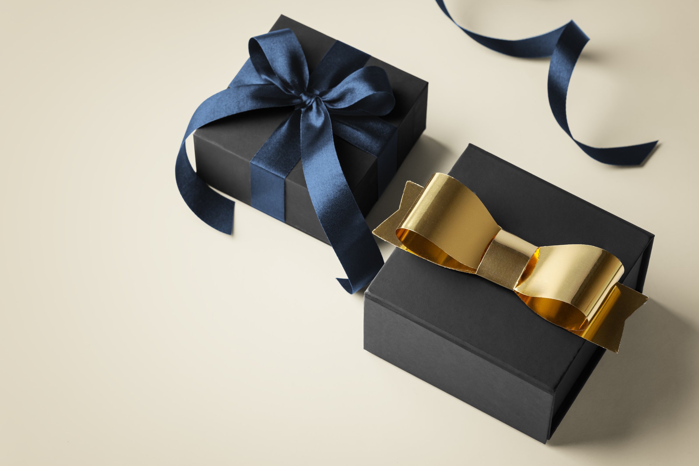 Black gift box with gold bow and blue ribbon on gold background, black friday concept, copy space