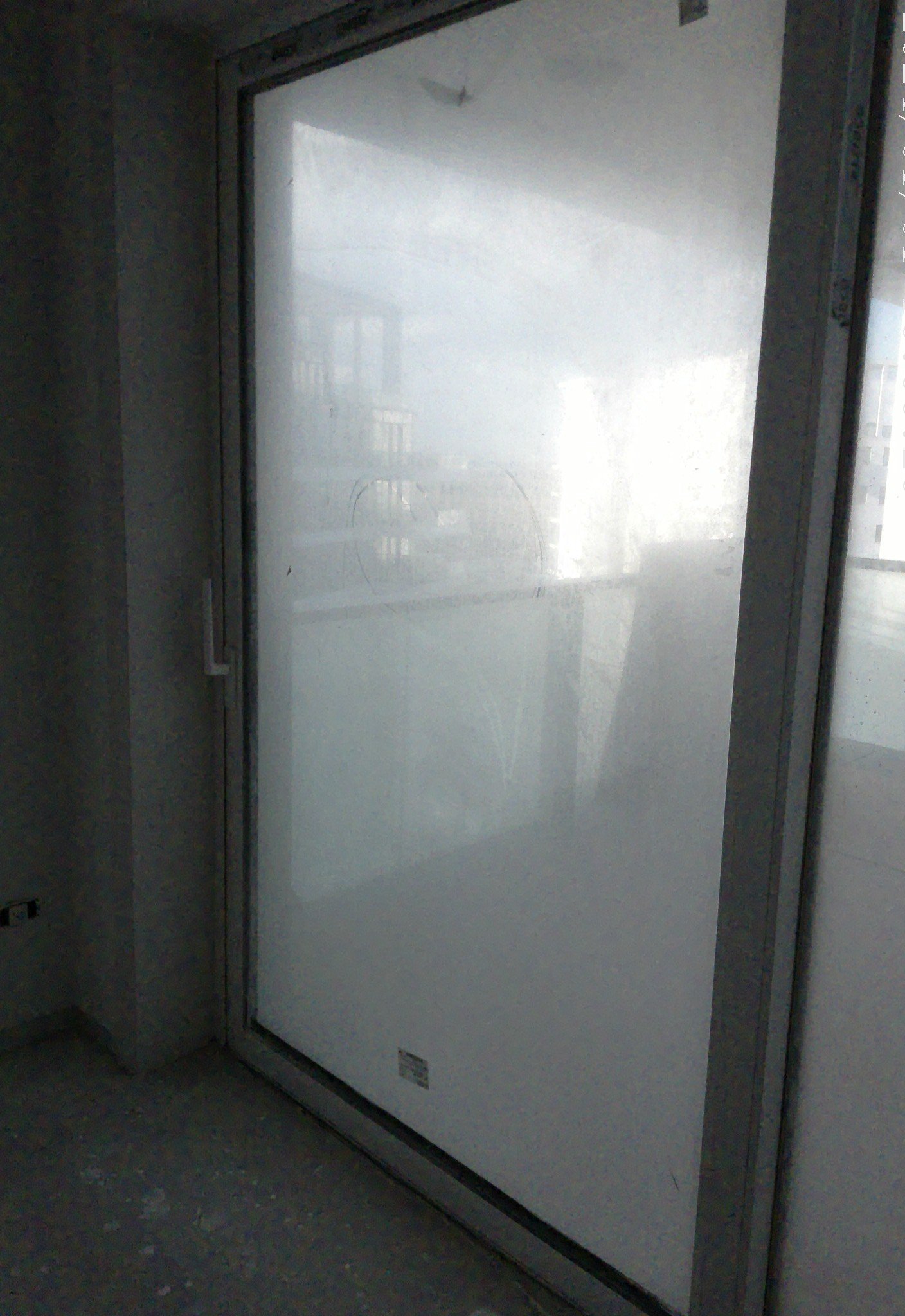 Fogged glass door with a blurred view of a balcony and cityscape in a dimly lit room.