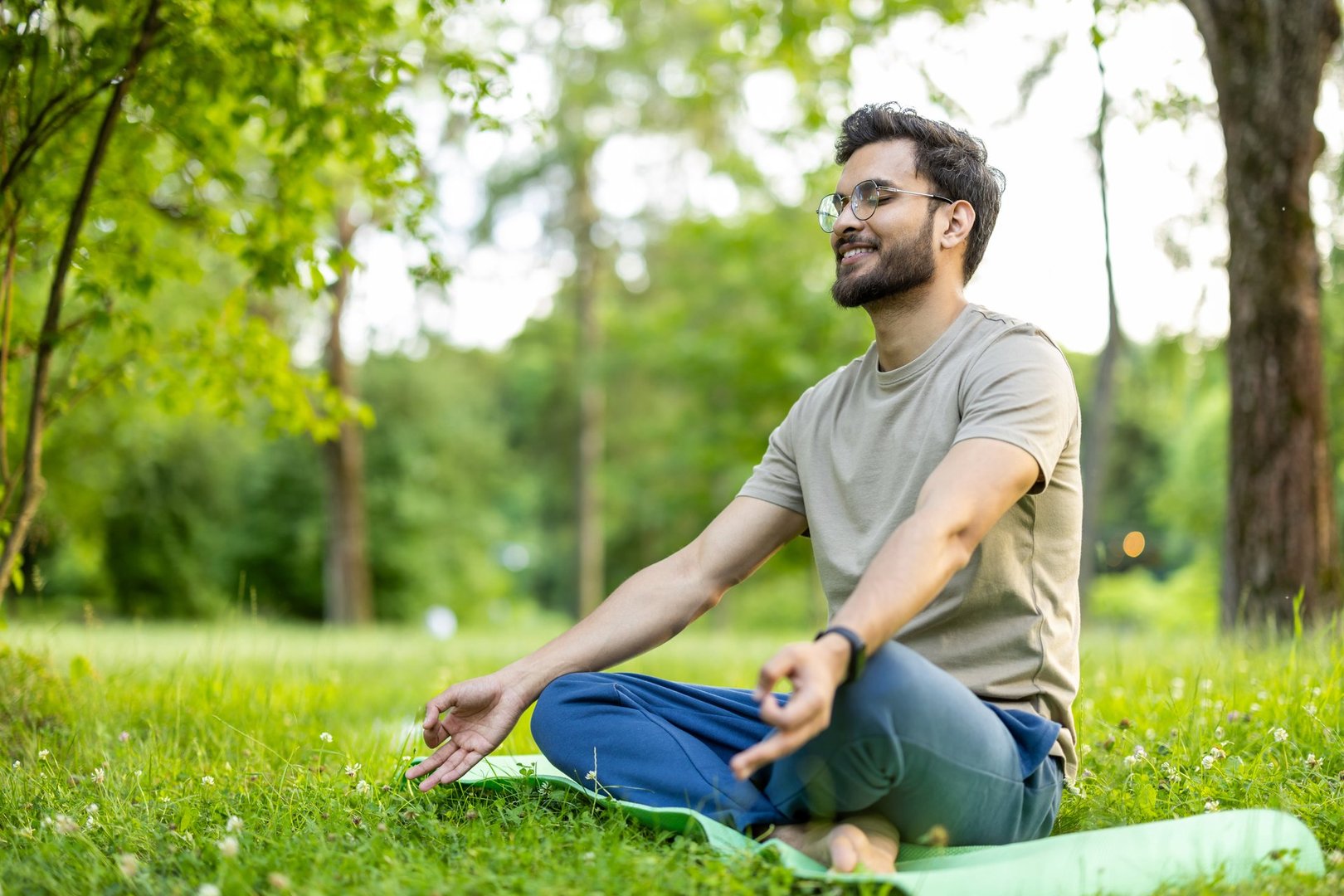 Man in park performing yoga meditation on mat. Person achieving relaxation and mindfulness in natural green environment. Feeling of tranquility and peace while practicing outdoor exercise.