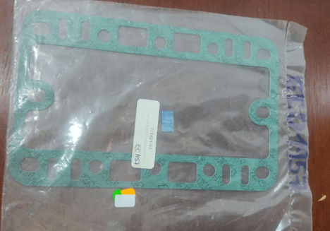 A green engine gasket in clear packaging with a barcode and product label on a wooden surface.