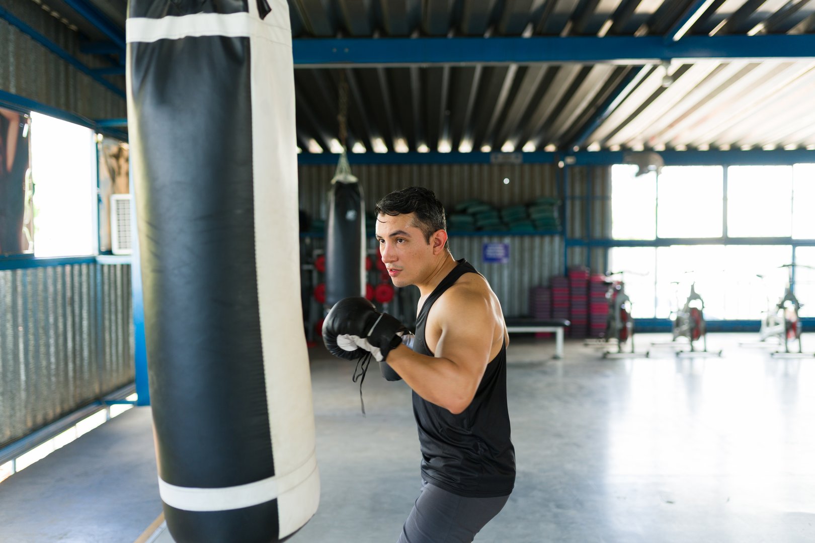 Athletic man performing boxing workout, punching a heavy bag in a gym. Focused boxer exercising for strength and fitness