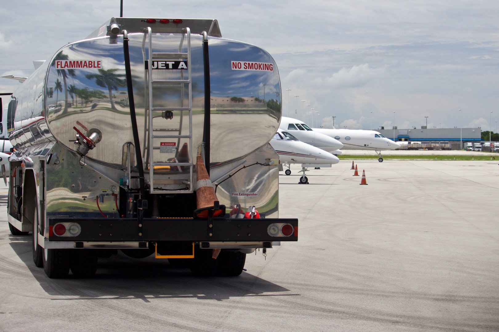 Tank truck on flight line with Jet A Fuel, no smoking, and hazmat placard on rear of tank, air field with business jets blurred in background