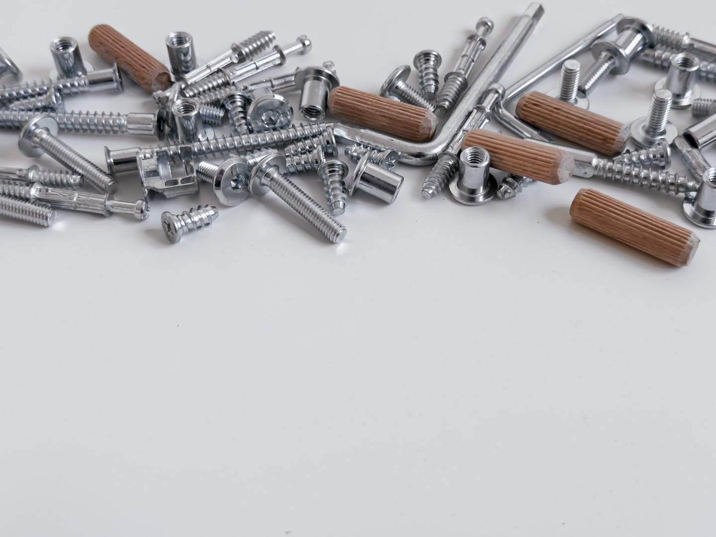 Assorted metal screws and dowels for furniture assembly on white background.