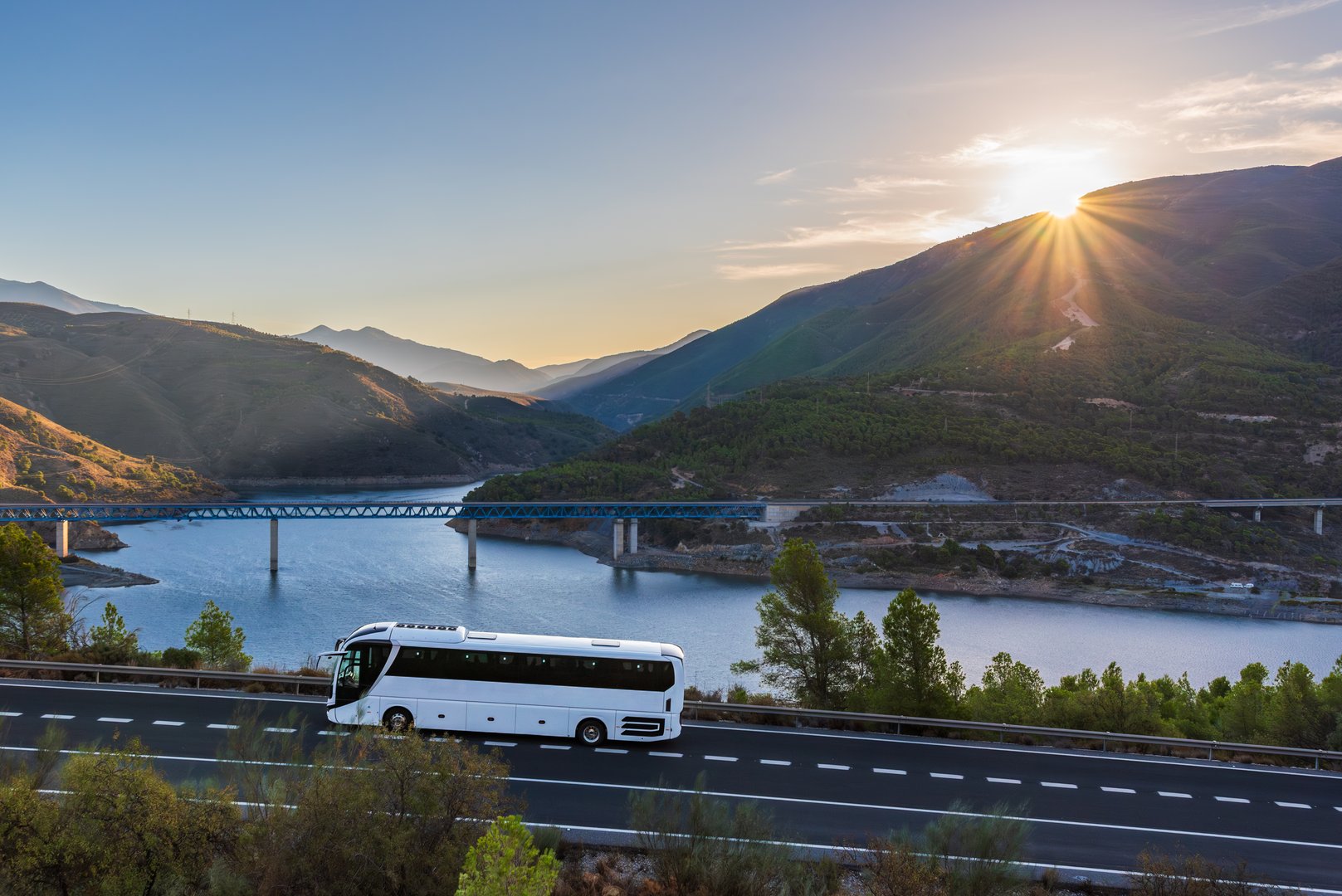 Bus on a mountain road with a reservoir and mountains