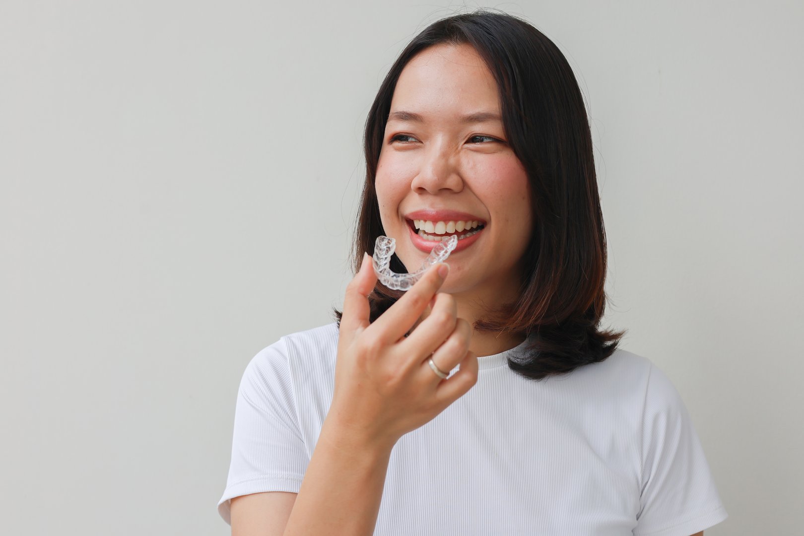 close up young lovely asian woman hand holding dental aligner retainer on white background for beautiful teeth content and dental treatment course concept