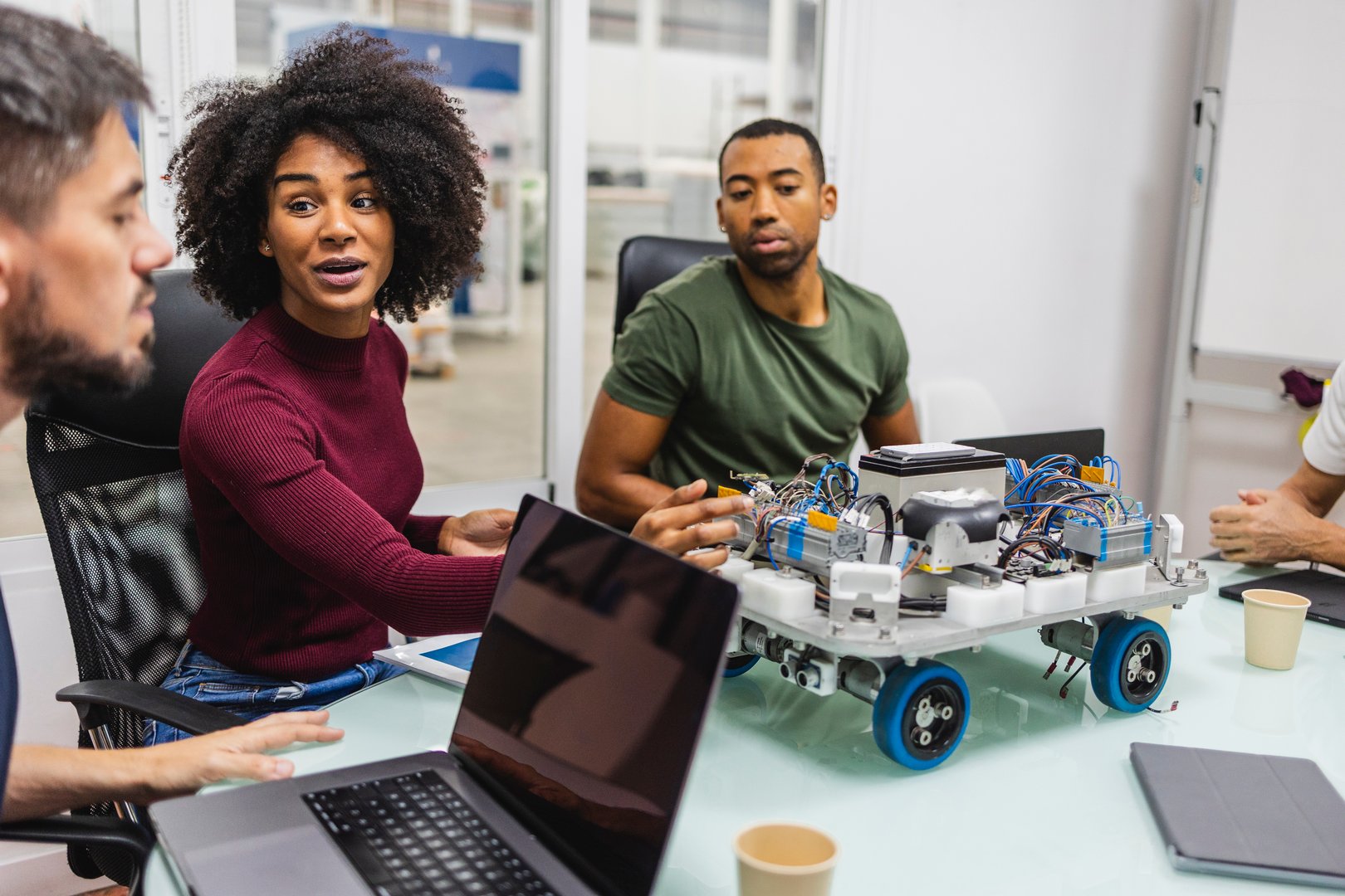 Multiracial team of engineers working together on a robotics project in a modern factory setting, discussing the design and functionality of a prototype robot