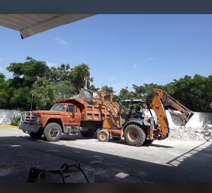 Construction site with an orange dump truck and backhoe loader moving debris under a clear blue sky.
