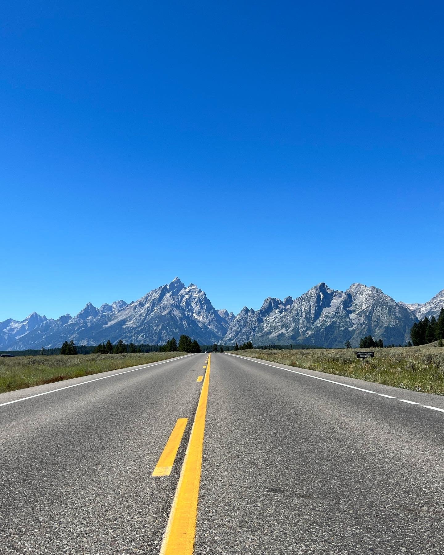 A straight road leading towards distant mountain range under a clear blue sky.