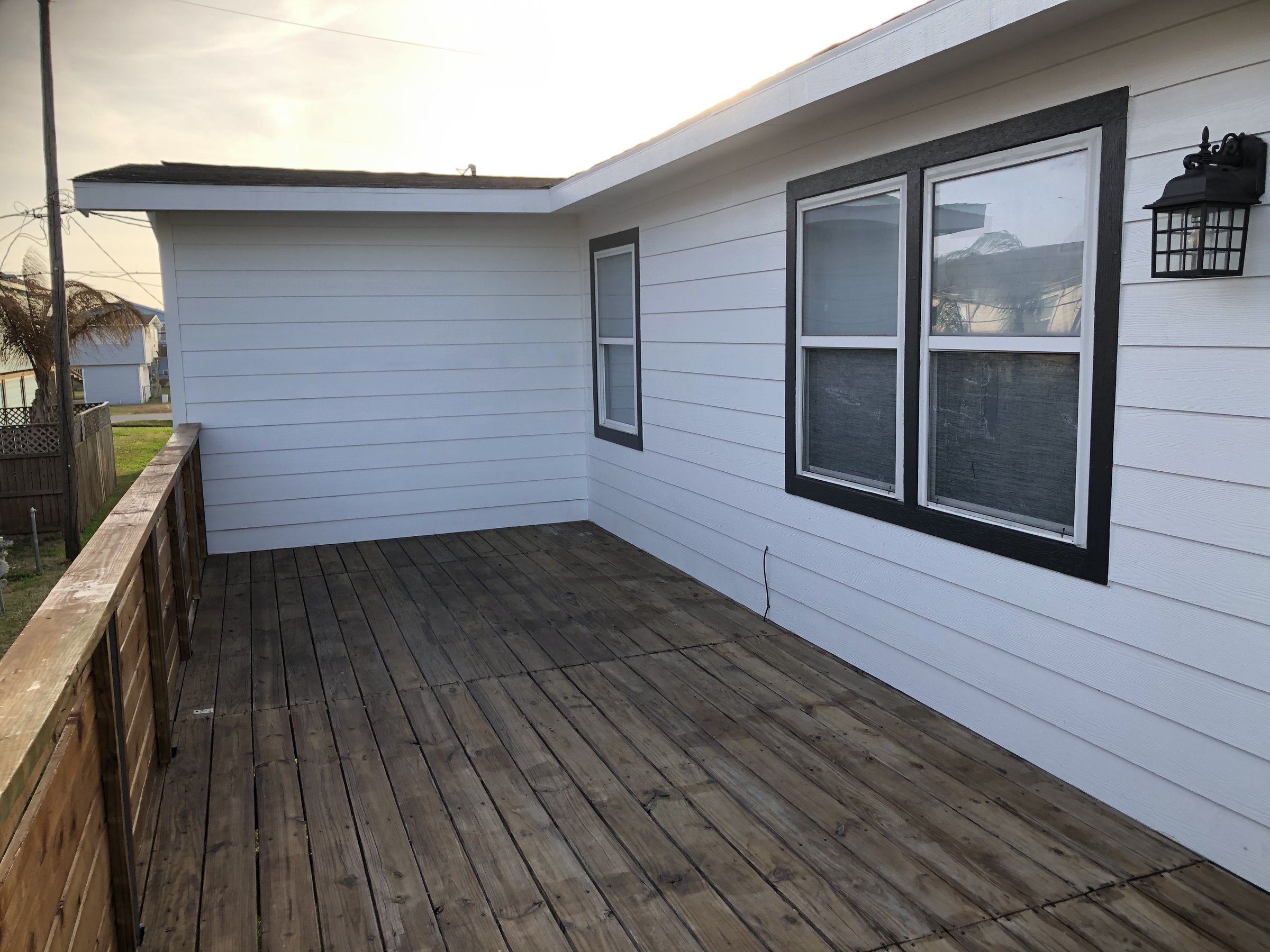 Wooden deck adjacent to a white house with black trim windows and a lantern-style outdoor light fixture.