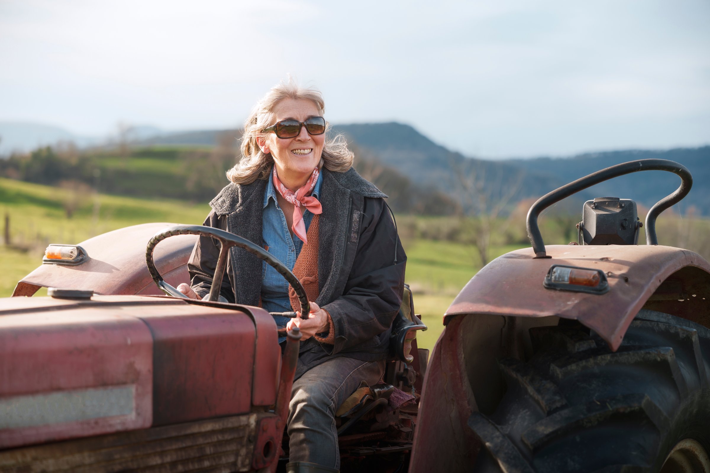 Mature female farmer driving a tractor in a field celebrates international workers' day