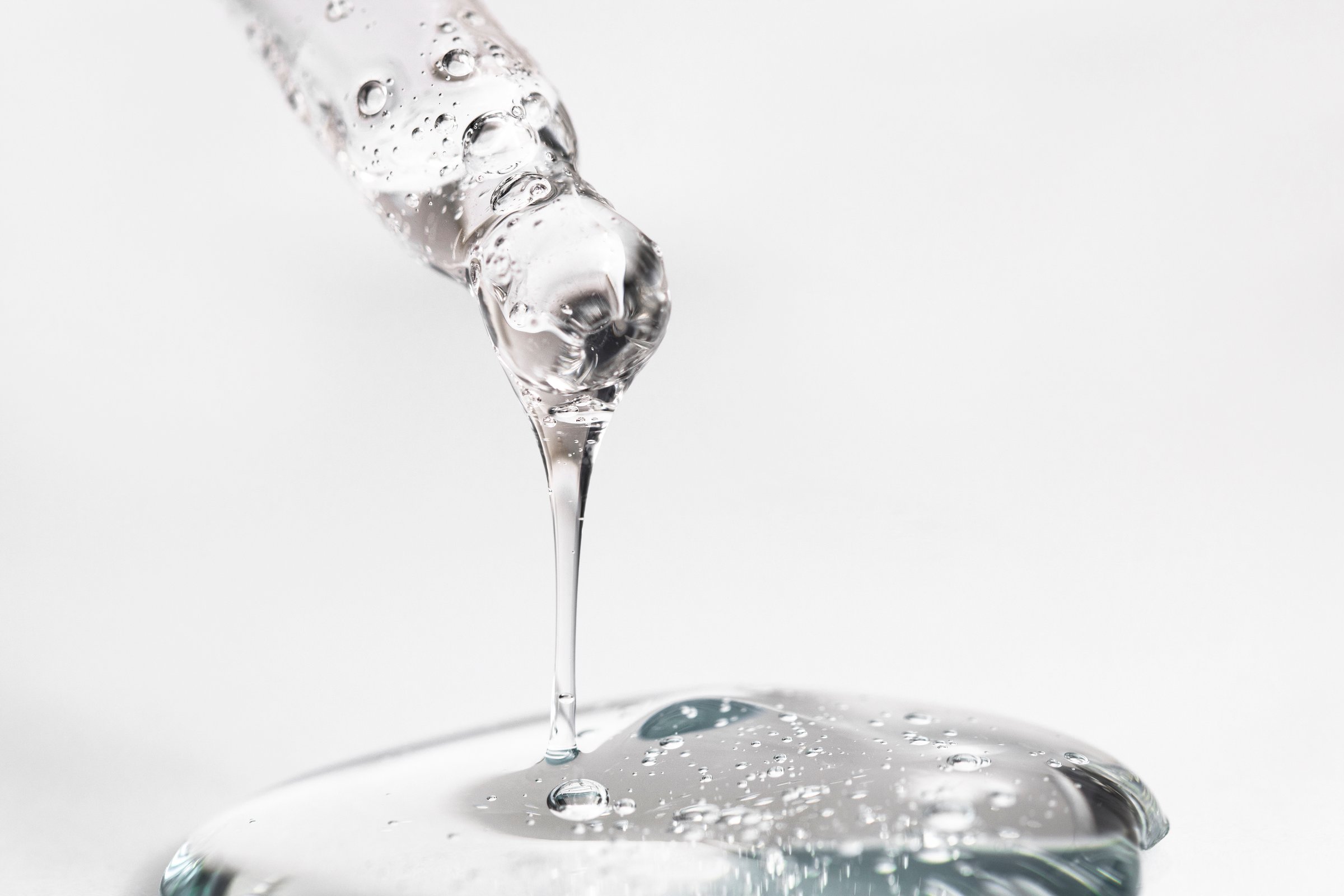 Hyaluronic acid in a glass pipette on a gray background macro. Transparent cosmetic texture with bubbles