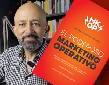 Person smiling next to a red book titled El Poderoso Marketing Operativo with a bookshelf in the background.