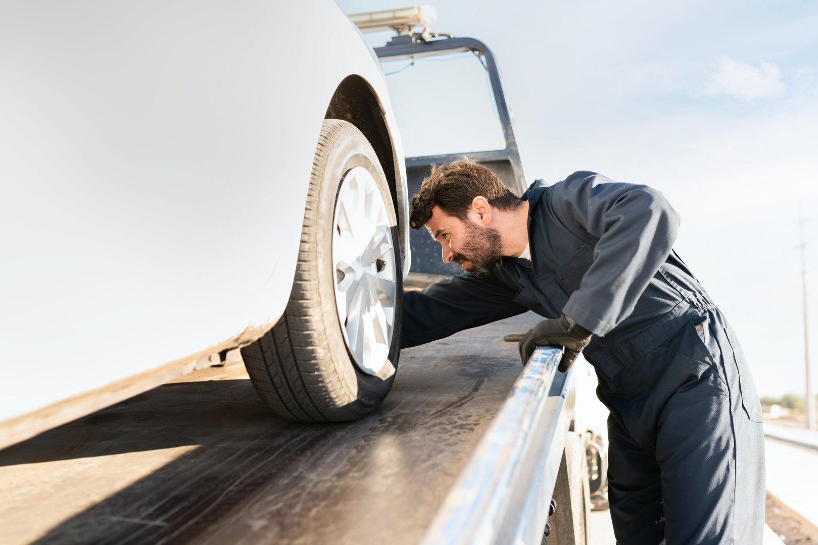 Side view of an operator checking on a broken-down vehicle on the plataform of the tow truck