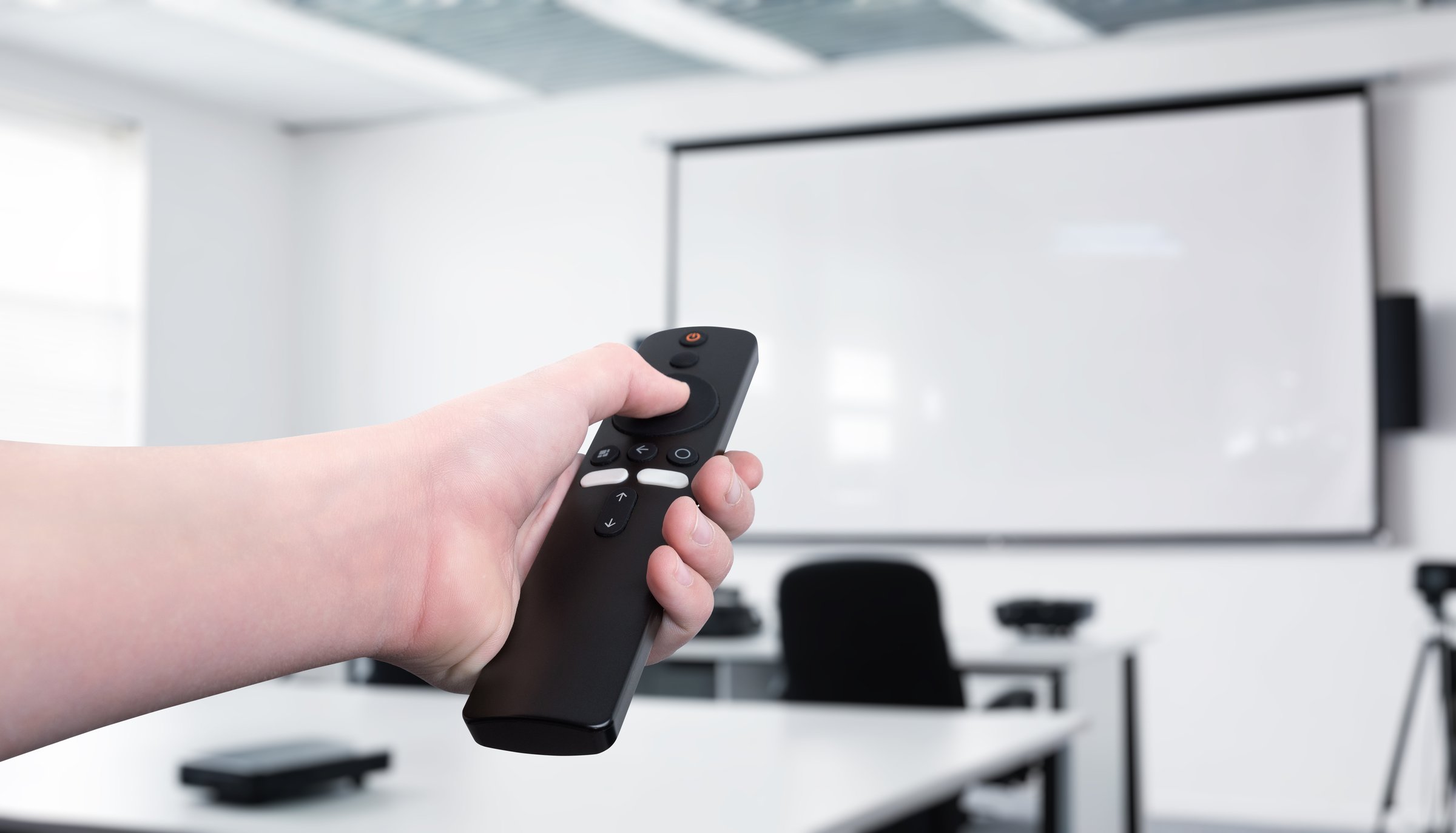Hand holding a remote control, operating a projector in a conference room or classroom. Concept of presentation control, business meeting, education, technology