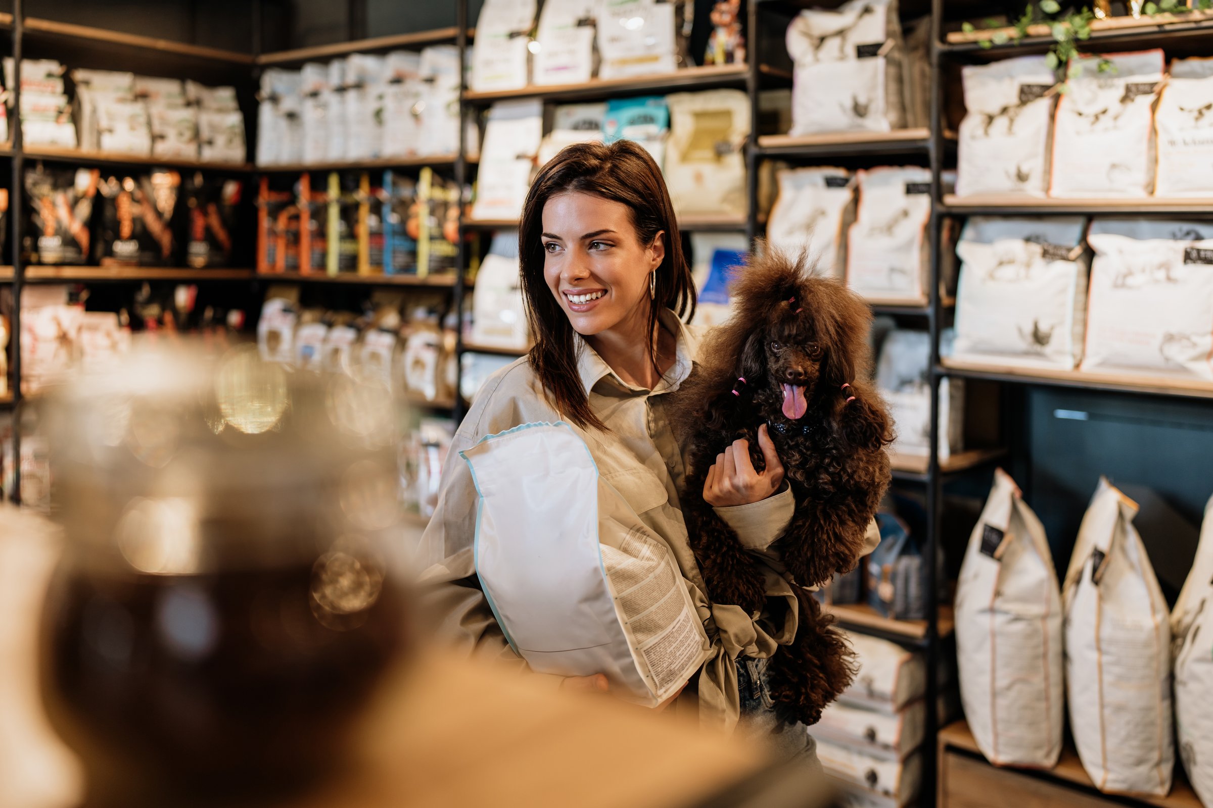 Beautiful young woman enjoying in modern pet shop together with her adorable brown toy poodle.