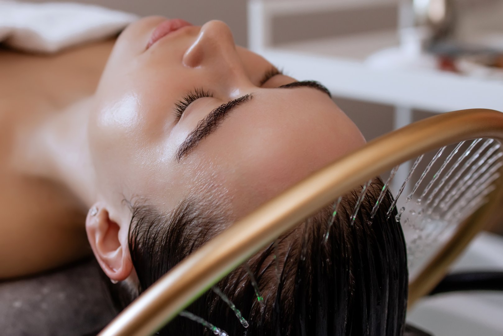 Close-up of a woman receiving a head massage during a Japanese head spa treatment with water flowing from a special hair washing tool, focusing on the scalp relaxation and beauty therapy