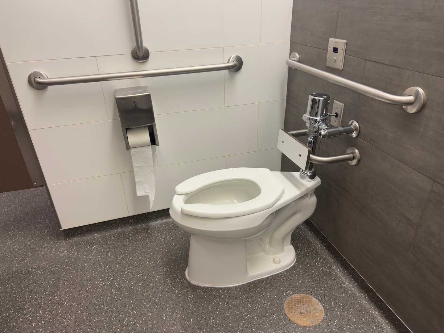 ADA-compliant restroom with support rails, wall-mounted toilet, automated flush system and sanitary fixtures, highlighting accessibility and modern facility standards.
