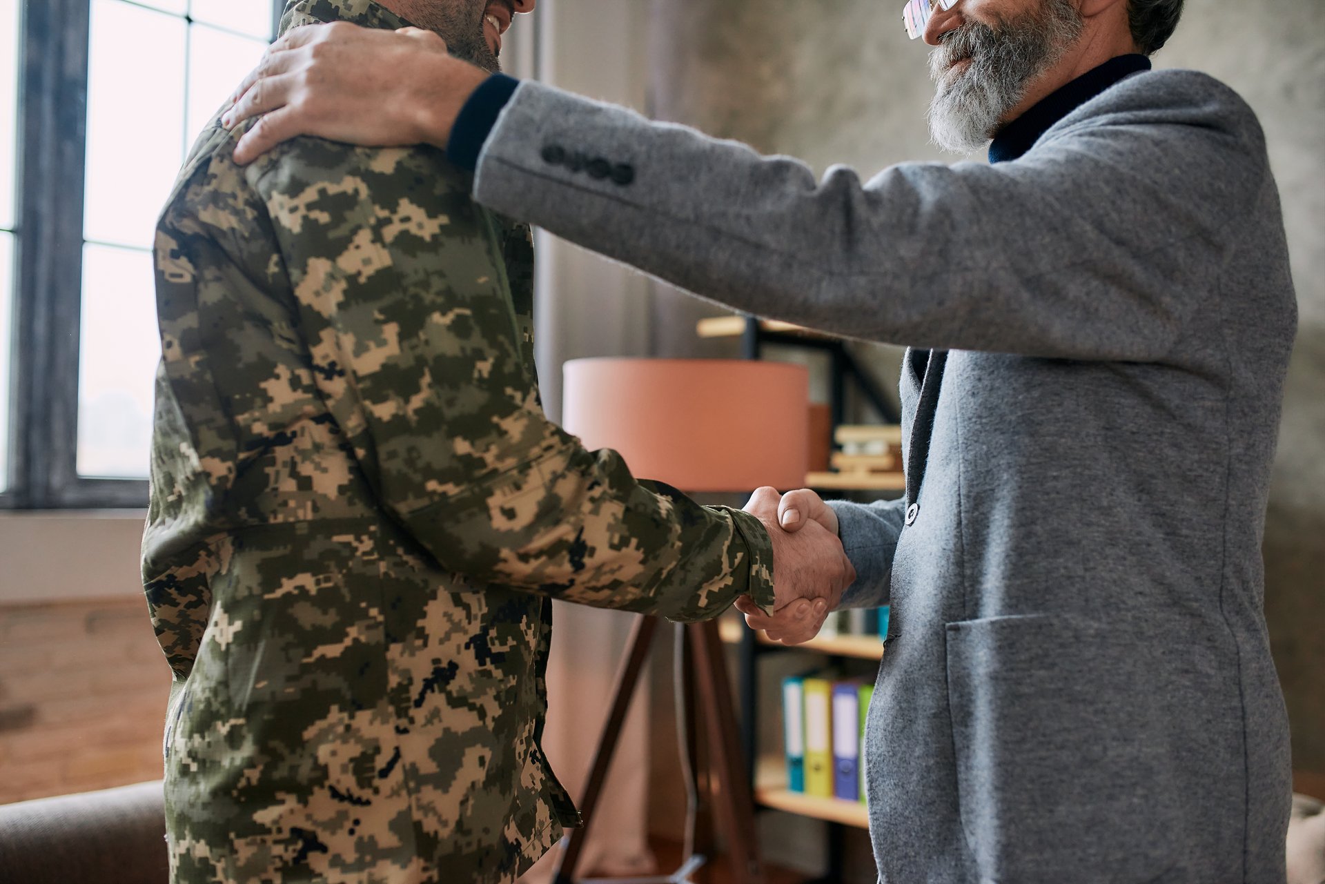 Cropped shot of mature psychologist smiling, shaking hands with middle aged military man after therapy session. Soldier suffering from depression, psychological trauma. PTSD concept. Focus on hands