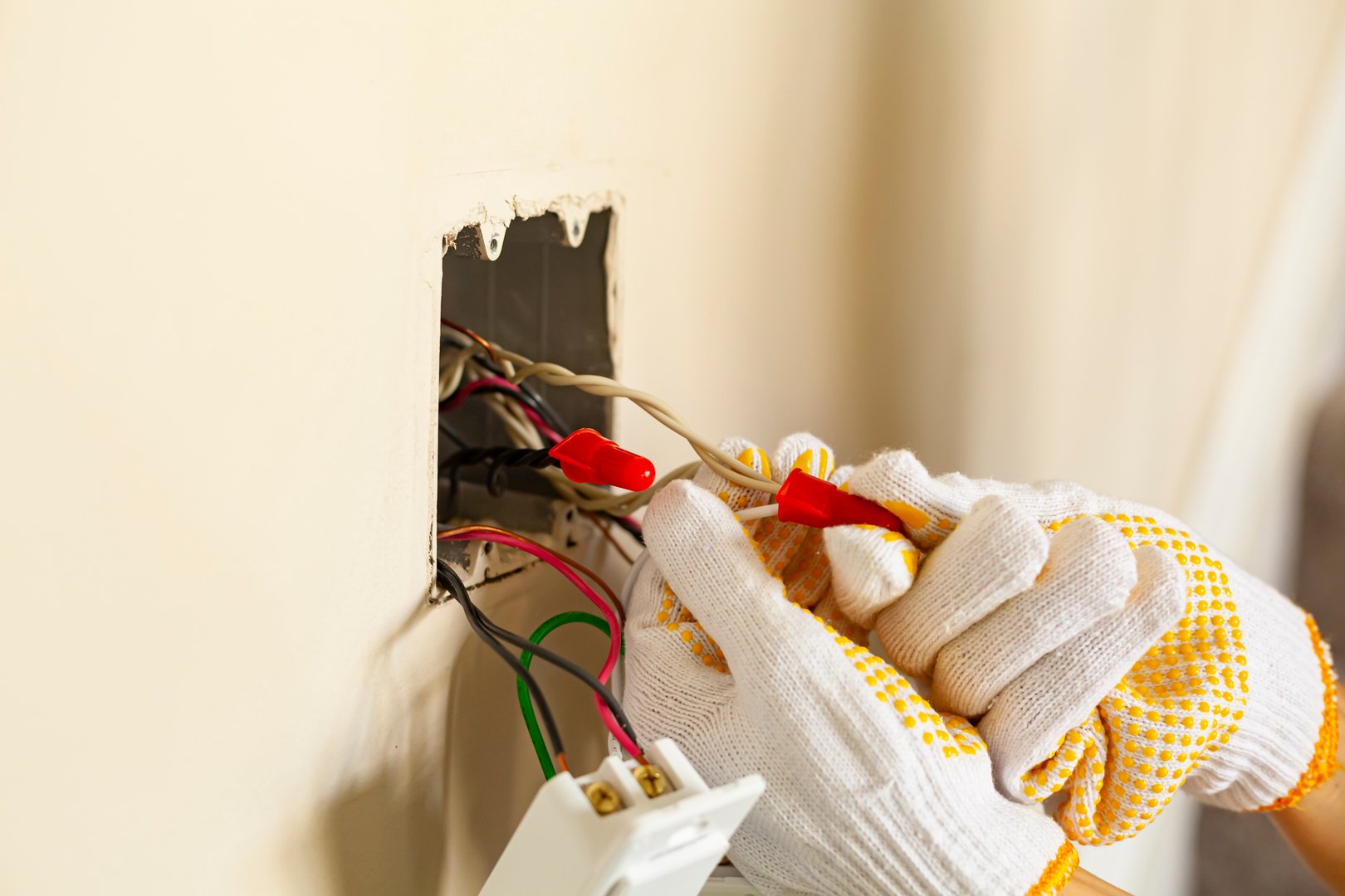 An electrician is replacing a wall switch. A DIY project concept. High voltage danger. The professional wearing shock proof gloves is tightening wirenuts