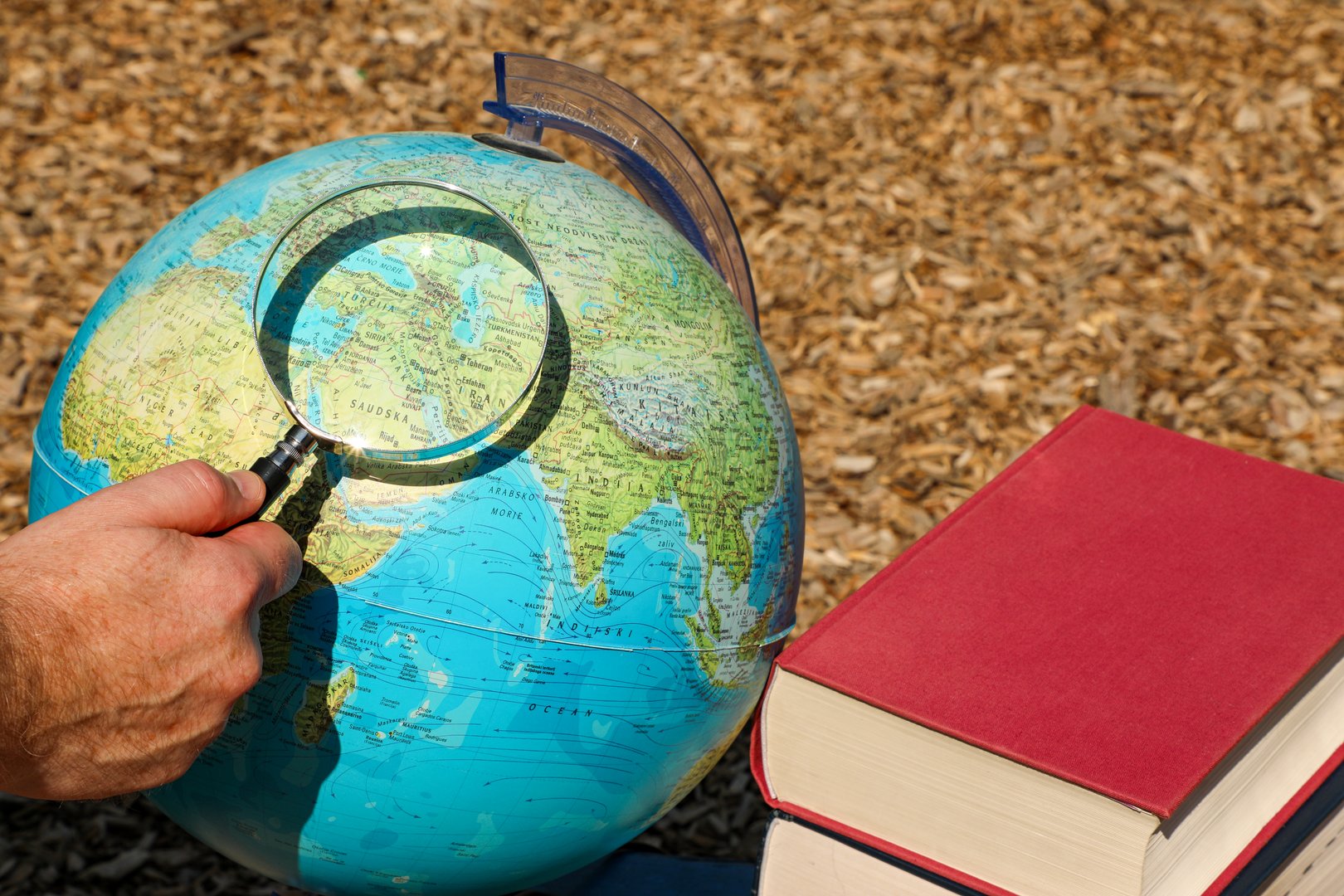A man holds a magnifying glass and carefully examines the inscription on the globe. Next to the globe are several large books for further study and choosing a travel direction.