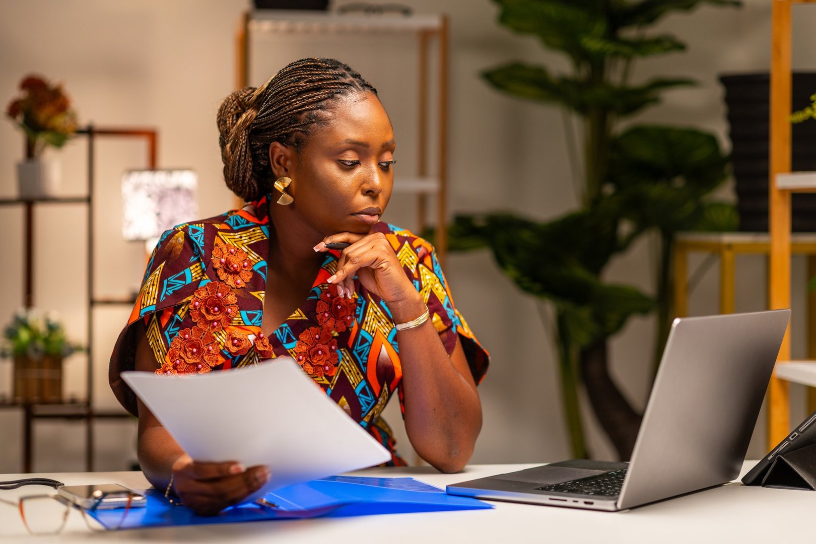 Focused African businesswoman reviewing documents while working on laptop