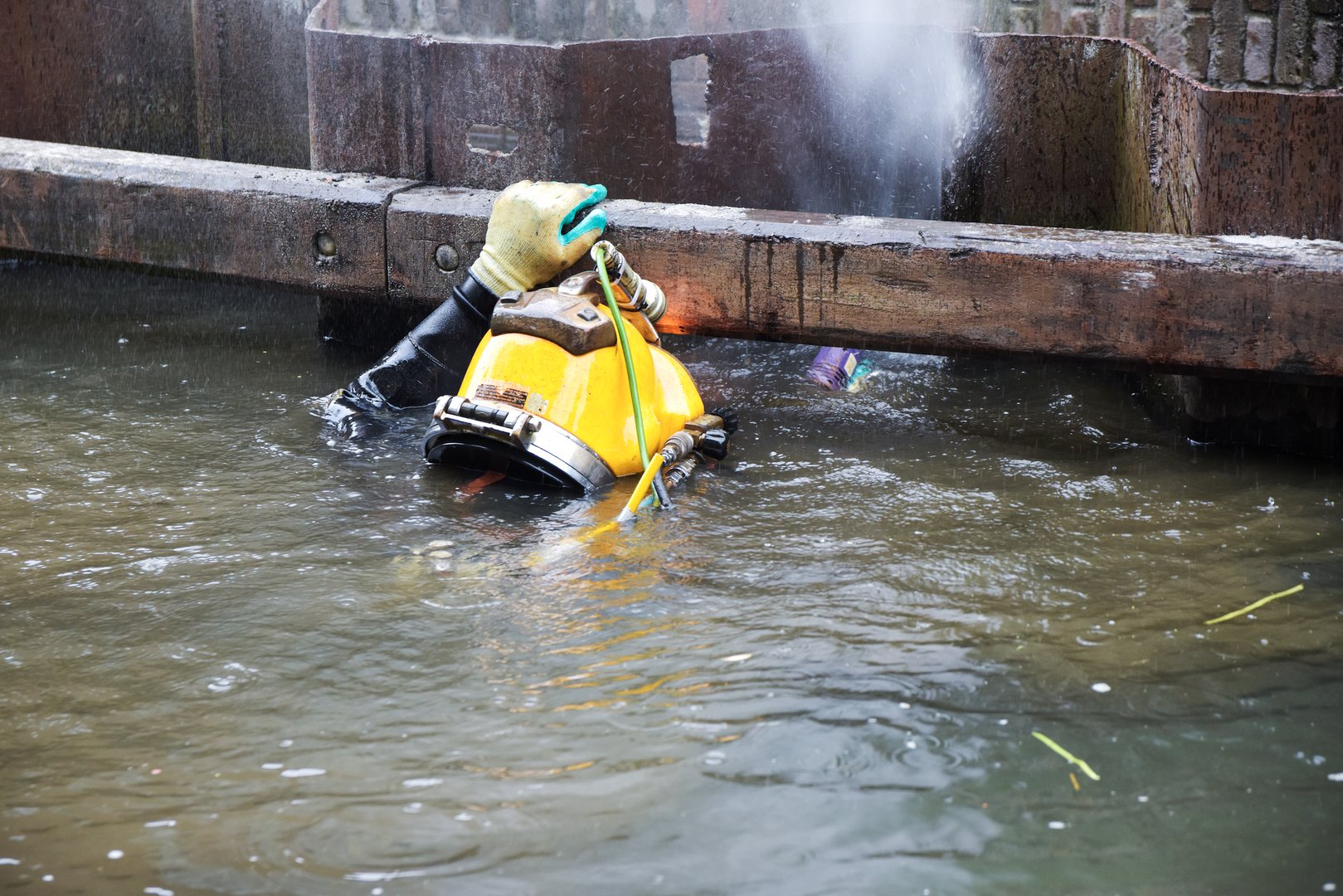 Diver with yellow helmet working in dirty water at the shore reinforcement in a canal, copy space