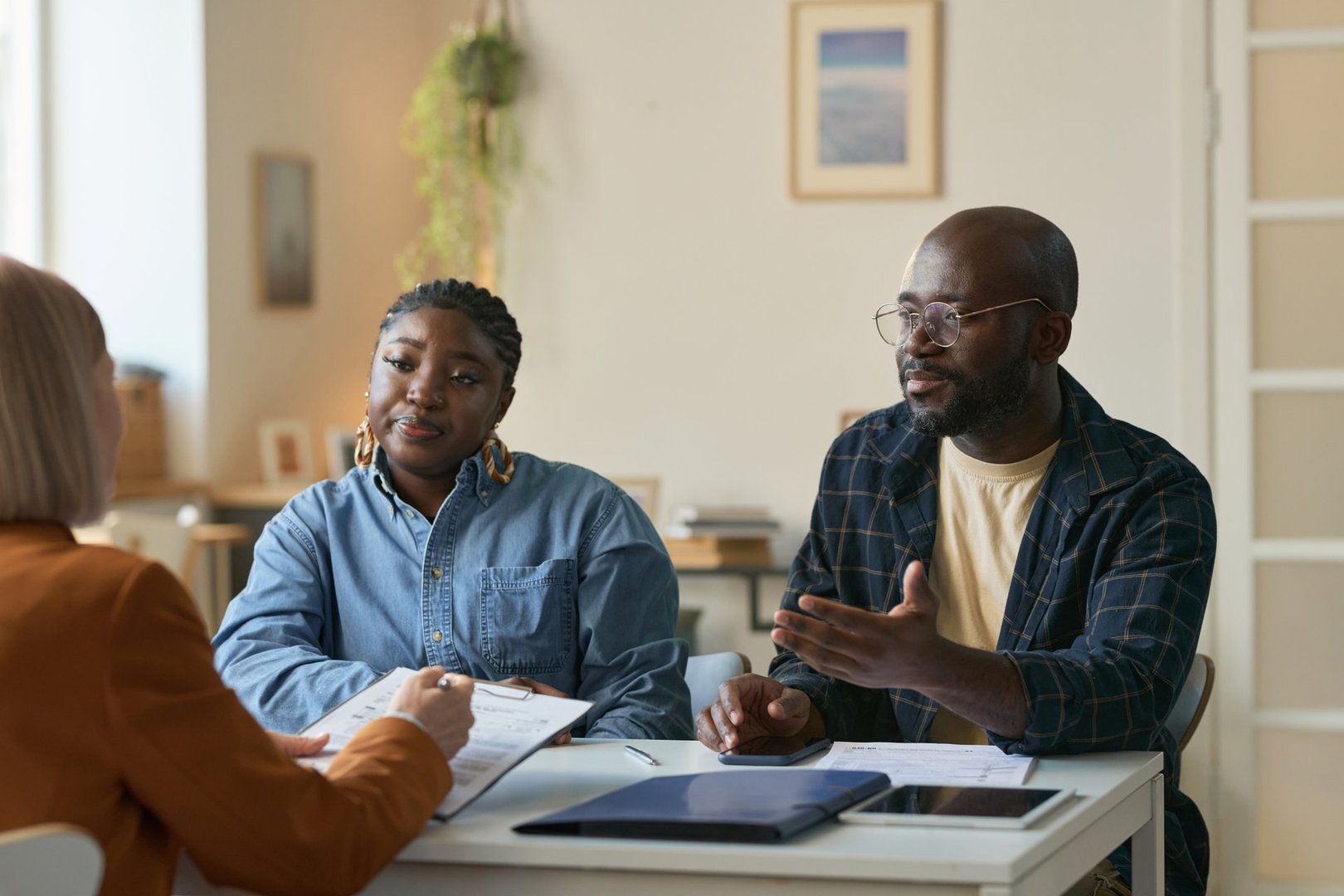 Portrait of adult African American couple talking to insurance agent during consultation while sitting at table in office copy space