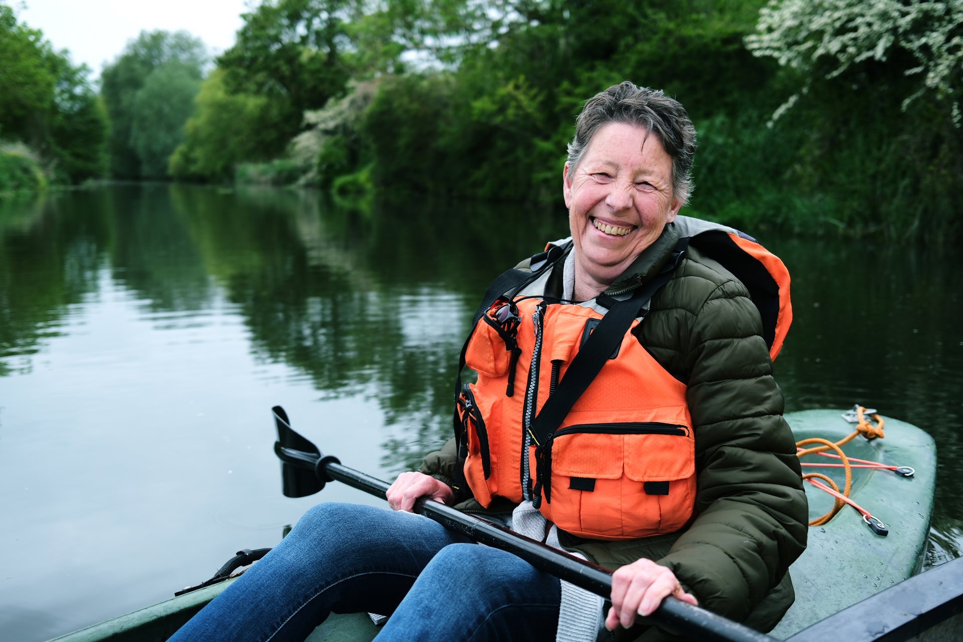 Happy senior woman in a life jacket enjoying a leisurely kayak trip on a peaceful river.