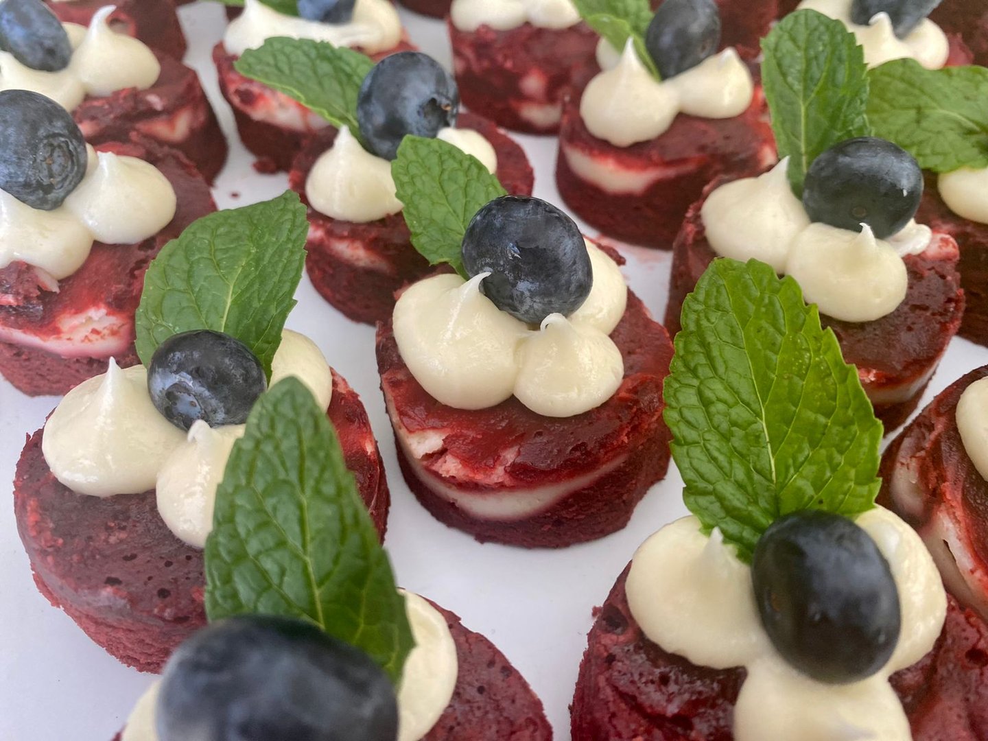 Mini red velvet cakes topped with creamy frosting, blueberries, and mint leaves.