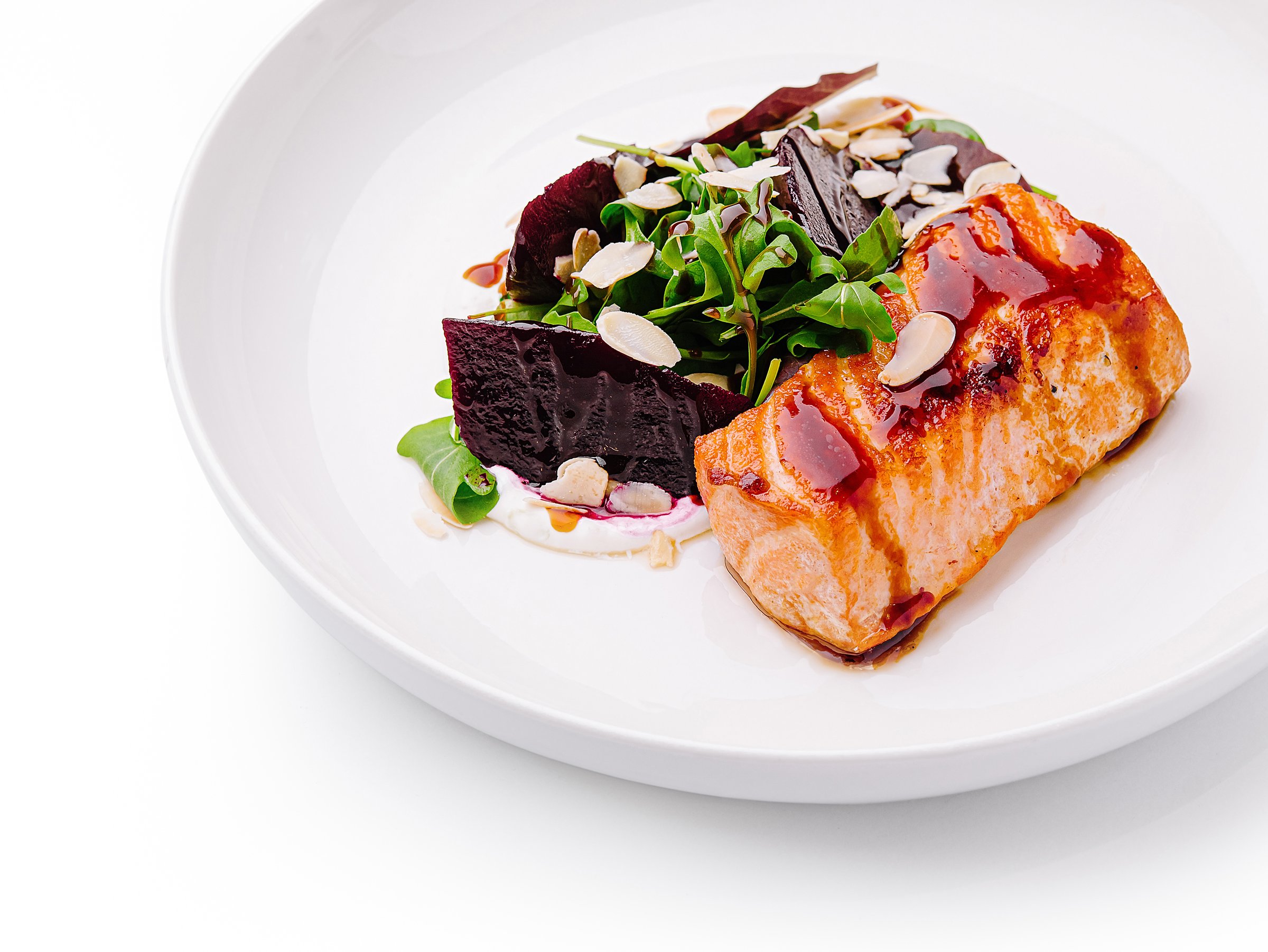 A delicious plate features a grilled salmon fillet served alongside fresh beetroot, leafy greens, and slivered almonds. The presentation emphasizes vibrant colors and textures.