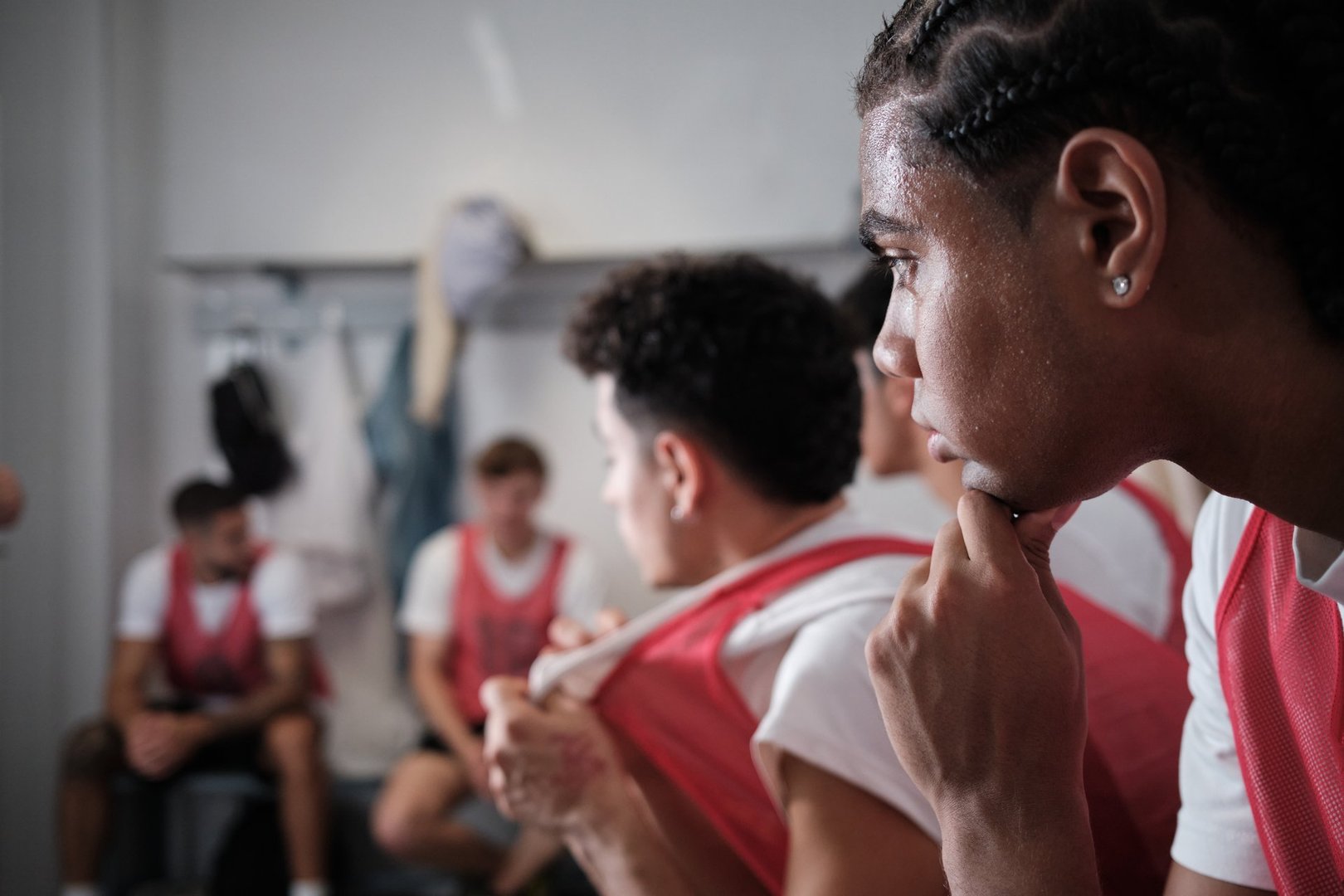 Young male athlete in uniform listening intently, reflecting on game strategy with his teammates in a sports locker room