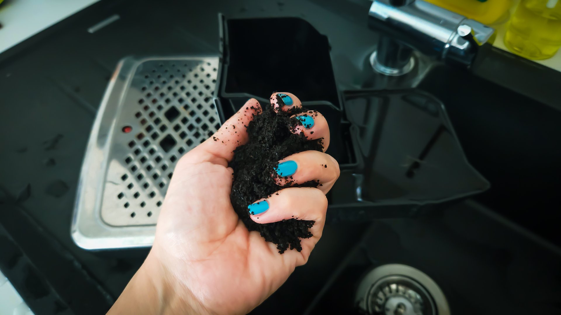 A hand with blue nail polish holds the leftover coffee grounds from the coffee machine.