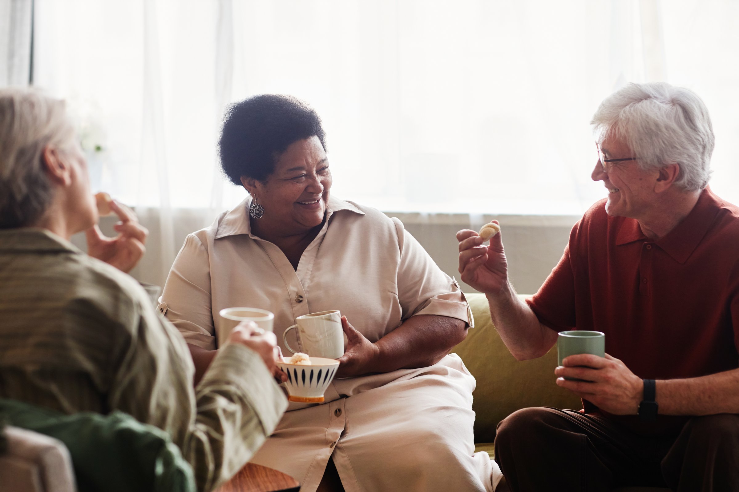 Candid cozy scene with group of senior people enjoying tea time together and chatting at home smiling happily