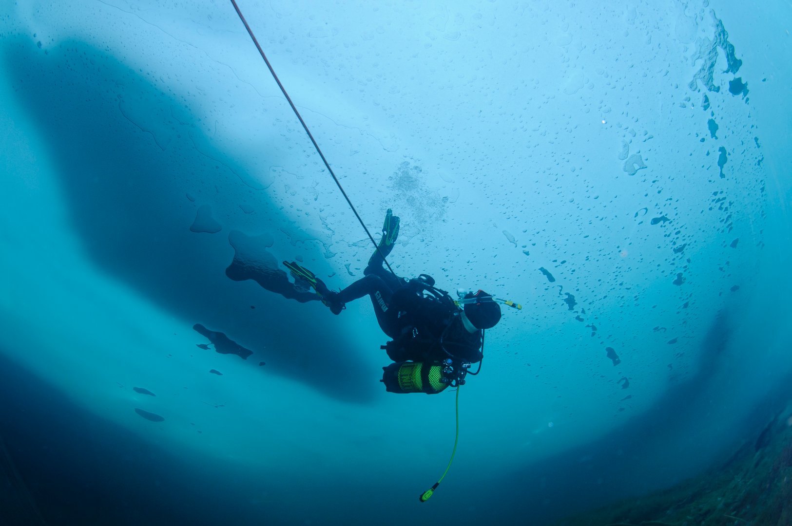 Scuba diver navigating the icy depths of a frozen lake in Panticosa, Spain, securely tethered to a safety line, embracing the thrill of underwater exploration in winter's chill