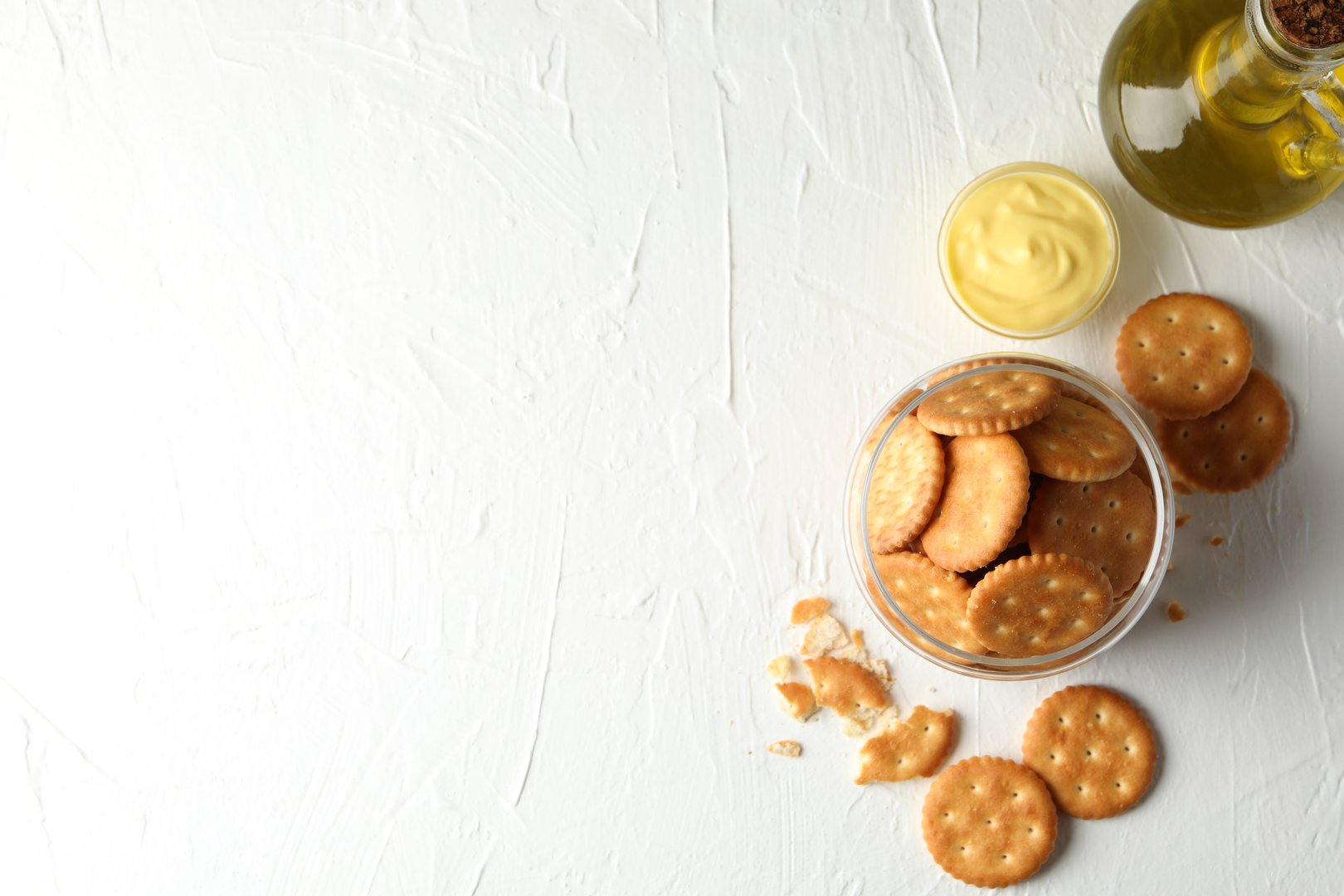Glass jar with crackers, sauce and oil on white table