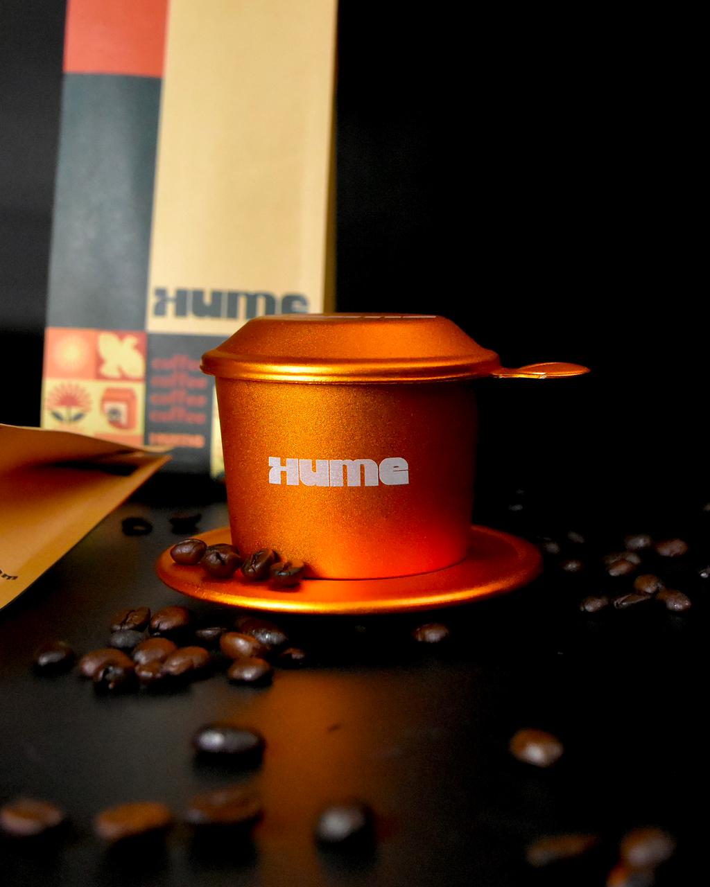Orange Hume coffee espresso cup with scattering coffee beans and a package in the background on a dark surface.