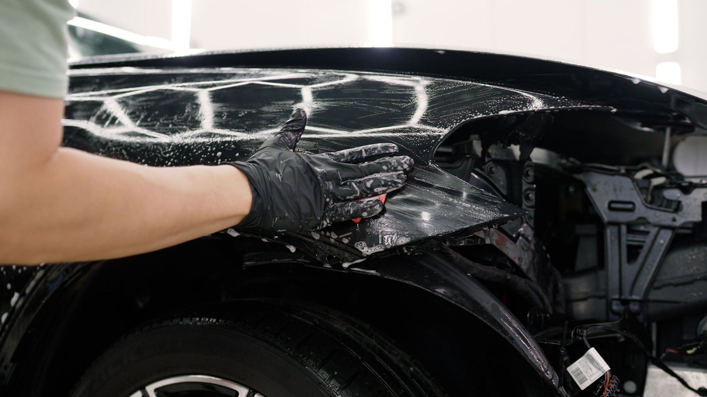Car detailer cleaning vehicle with sponge and detergent, ensuring thorough cleaning and paint protection during detailing process