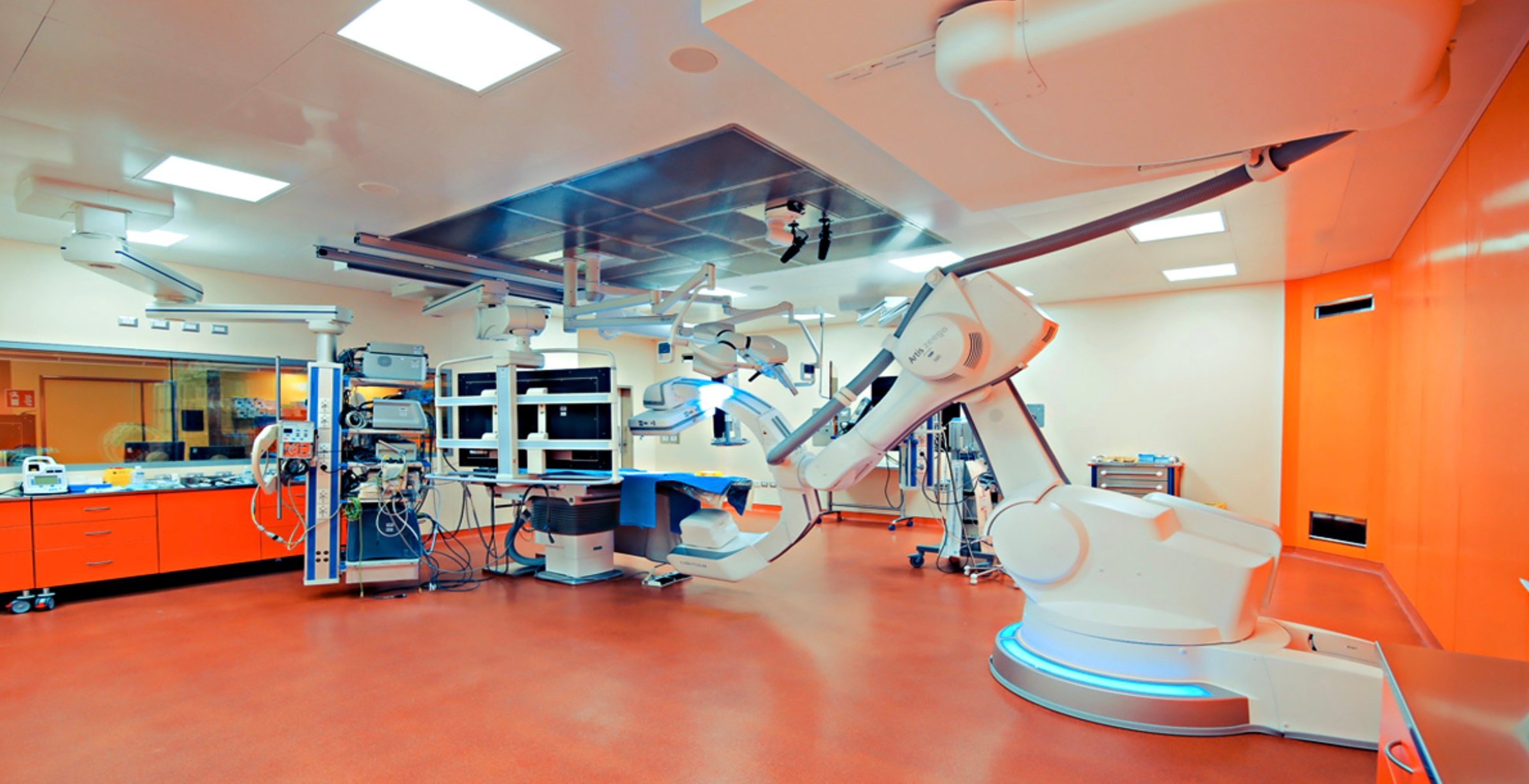 Modern operating room with advanced robotic surgical equipment and orange accents.
