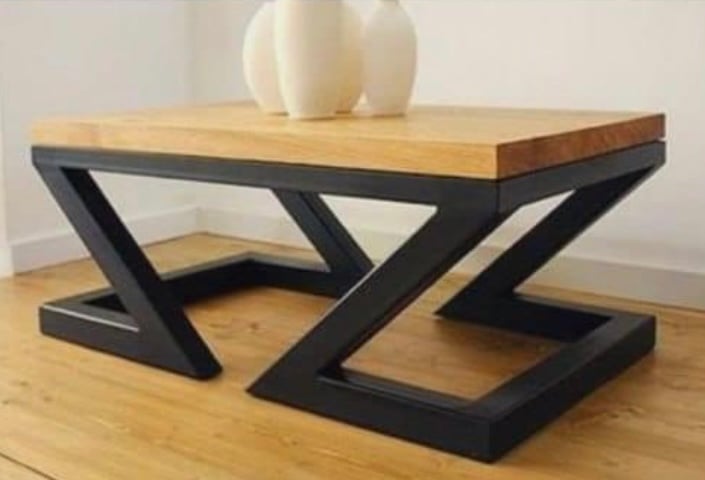 Modern coffee table with wooden top and angular black metal base on a wooden floor.