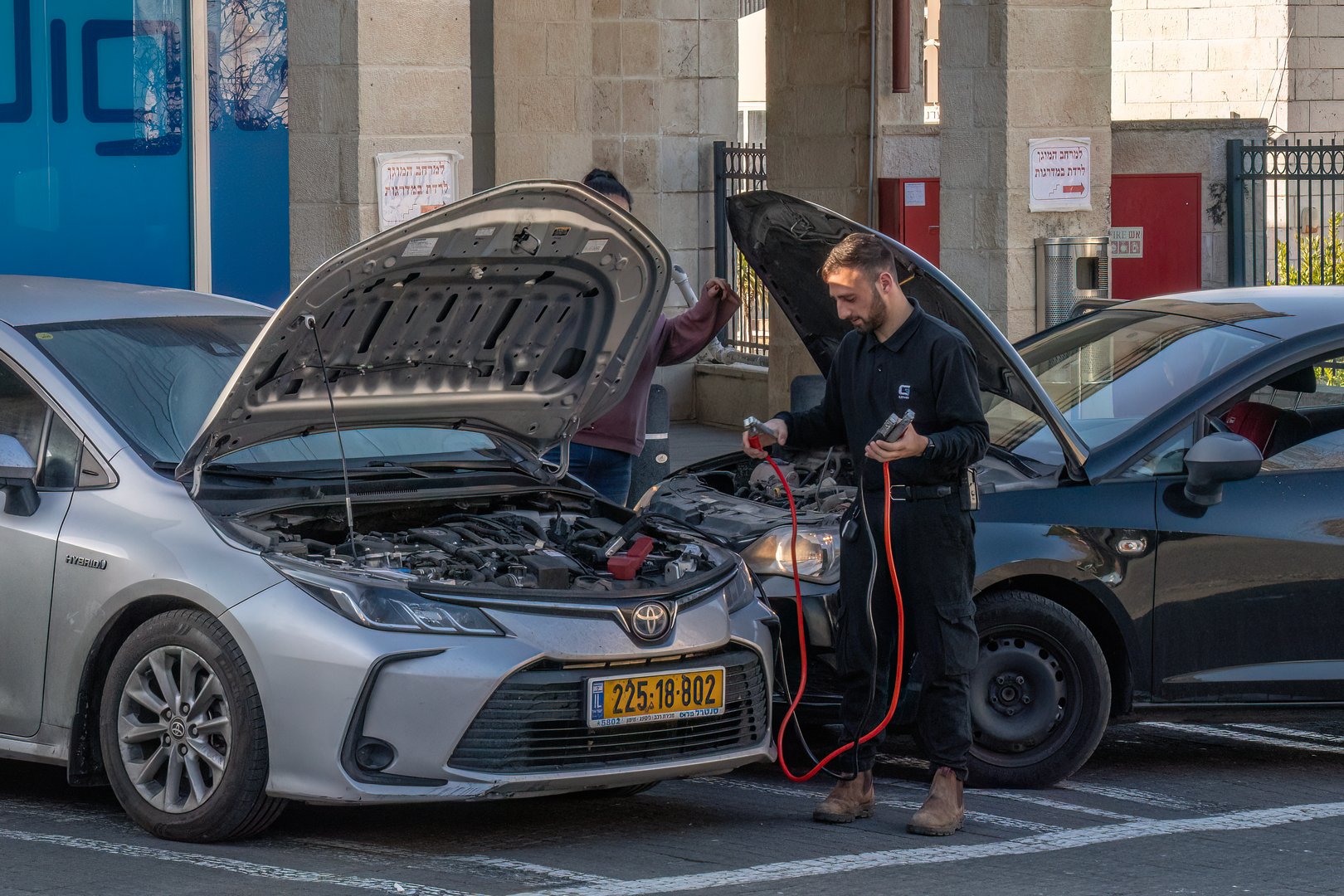 Mevasseret Zion, Israel - March 14th, 2024: A man jump starting a car with a dead battery, on a city street.