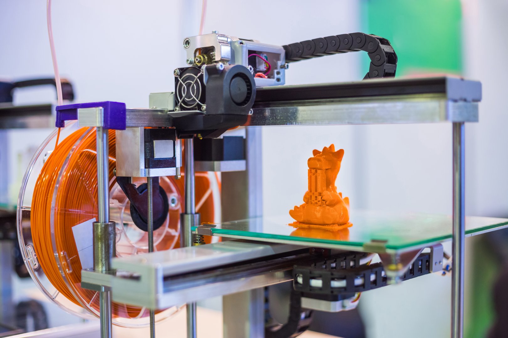 Automatic 3D printer machine printing plastic model of orange toy dragon at modern technology exhibition. 3D printing, additive technologies, 4.0 industrial revolution and futuristic concept