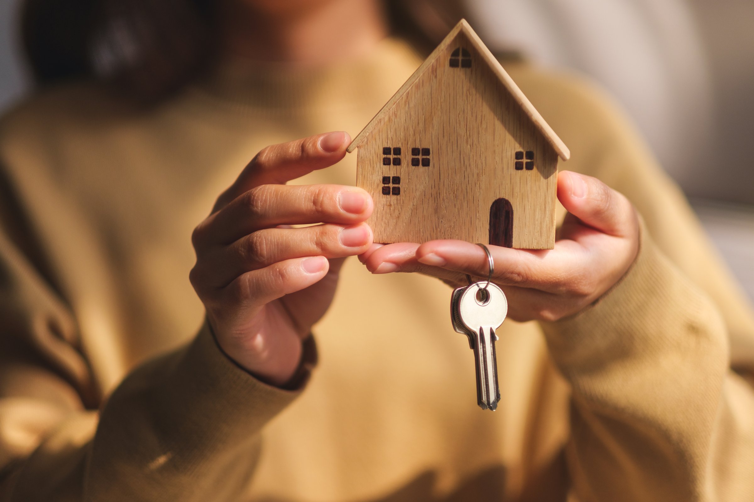 Closeup image of a woman holding a wooden house model and the keys for real estate concept