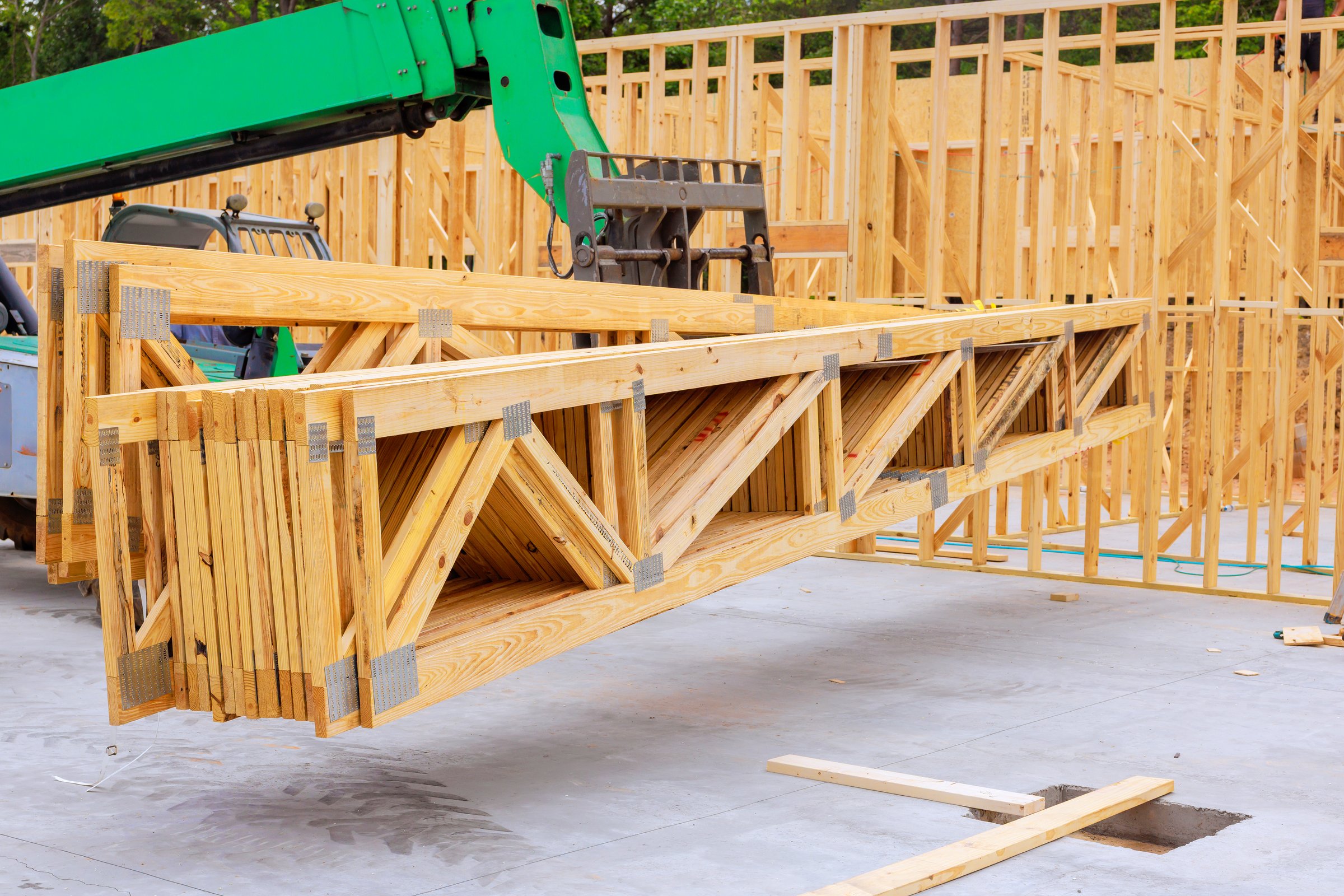 Telehandler crane raises wooden trusses at construction site during frame assembly building process.