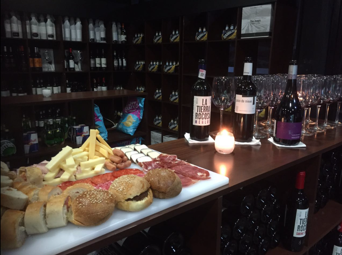Wine tasting setup with bottles, glasses, and a platter of assorted cheeses, meats, and breads on a wooden table.