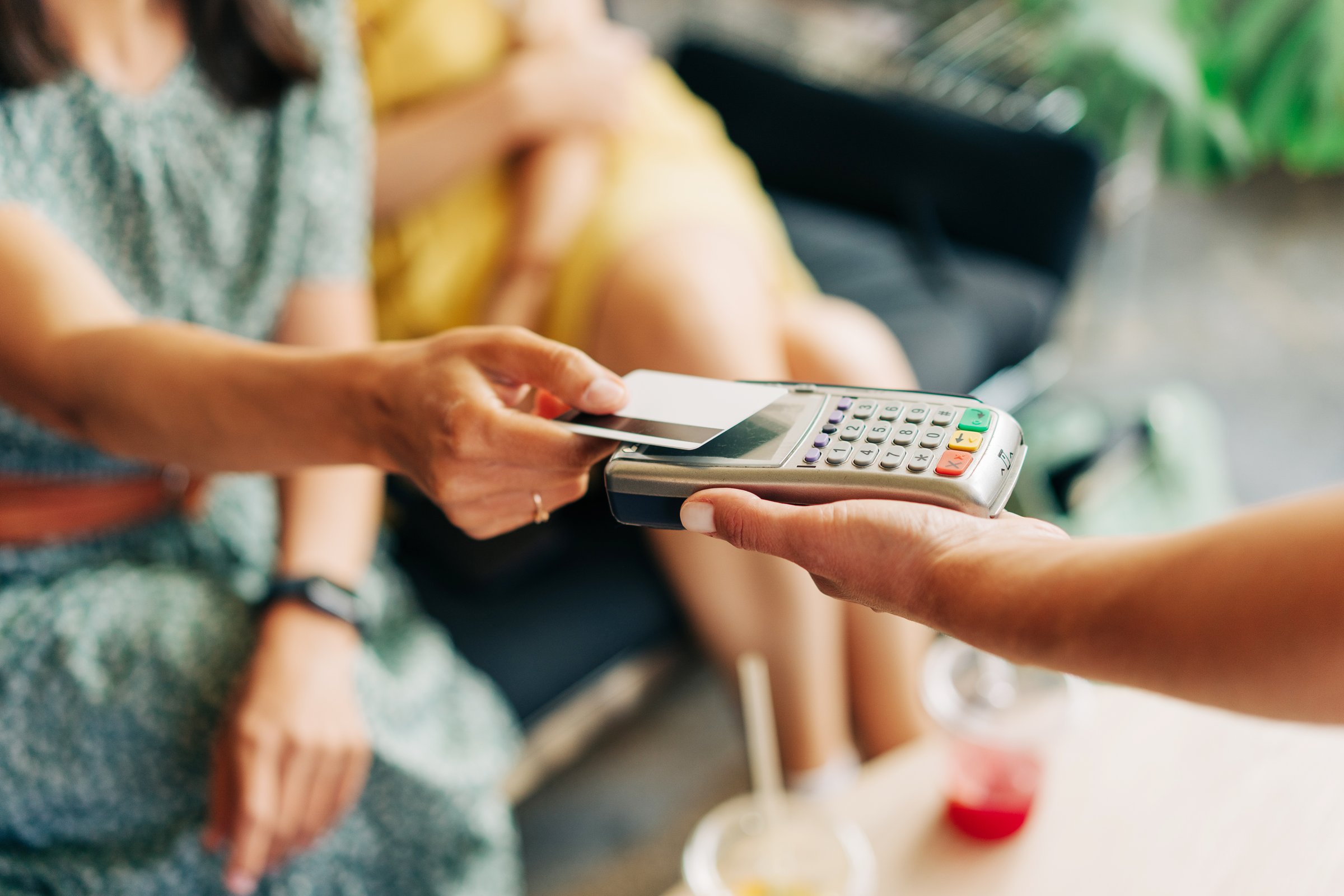 Unrecognizable women pay with a credit card in a cafe.