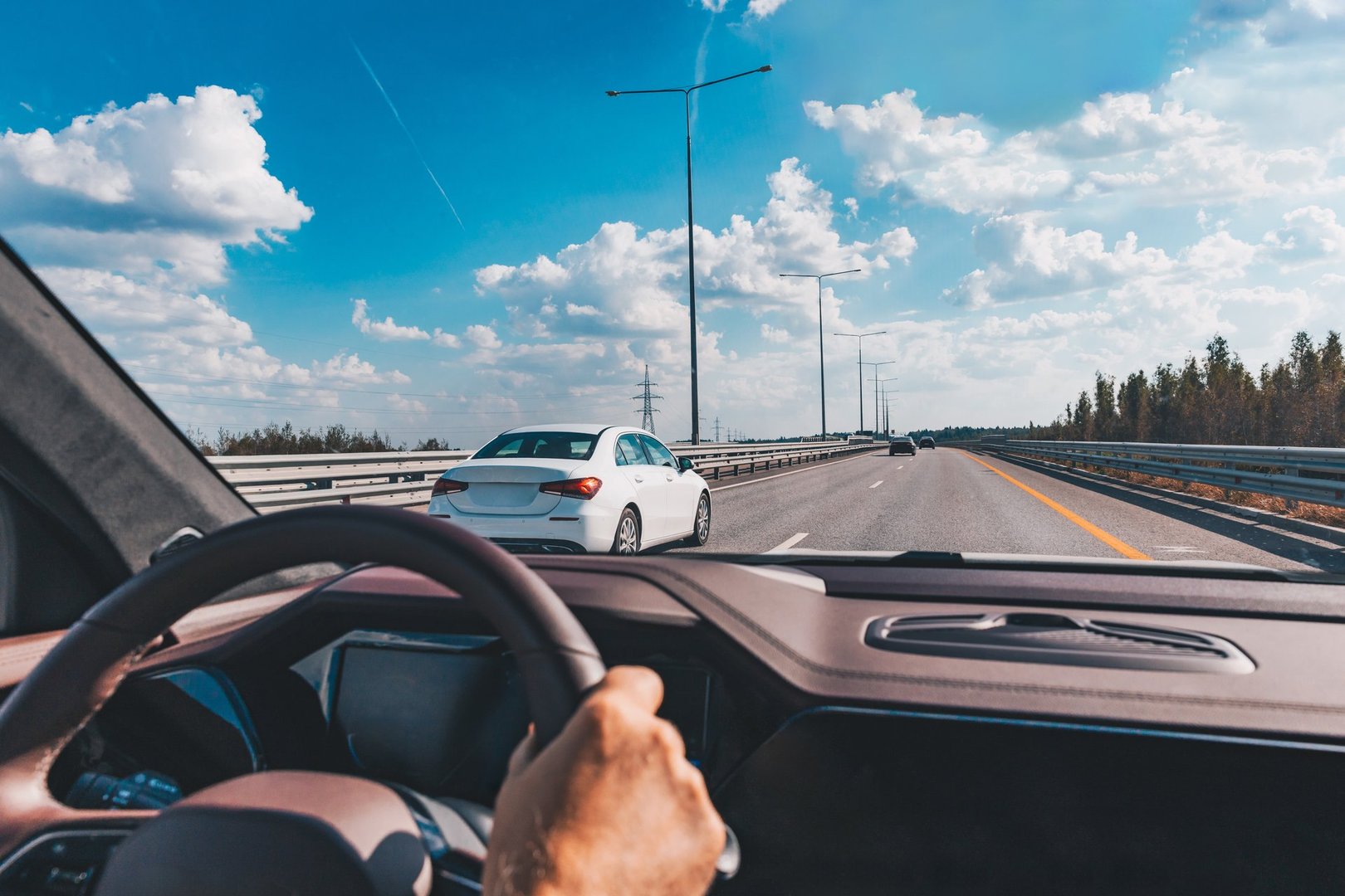 Man driving modern car from rear view on the highway. Hands on the steering wheel.